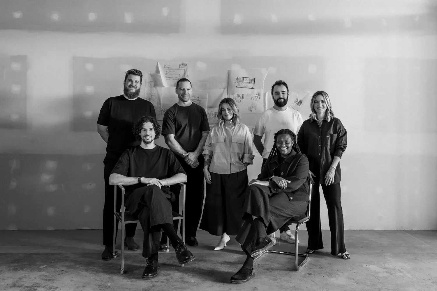 Black-and-white portrait of the Dalecki Design team gathered in their studio in front of architectural sketches.
