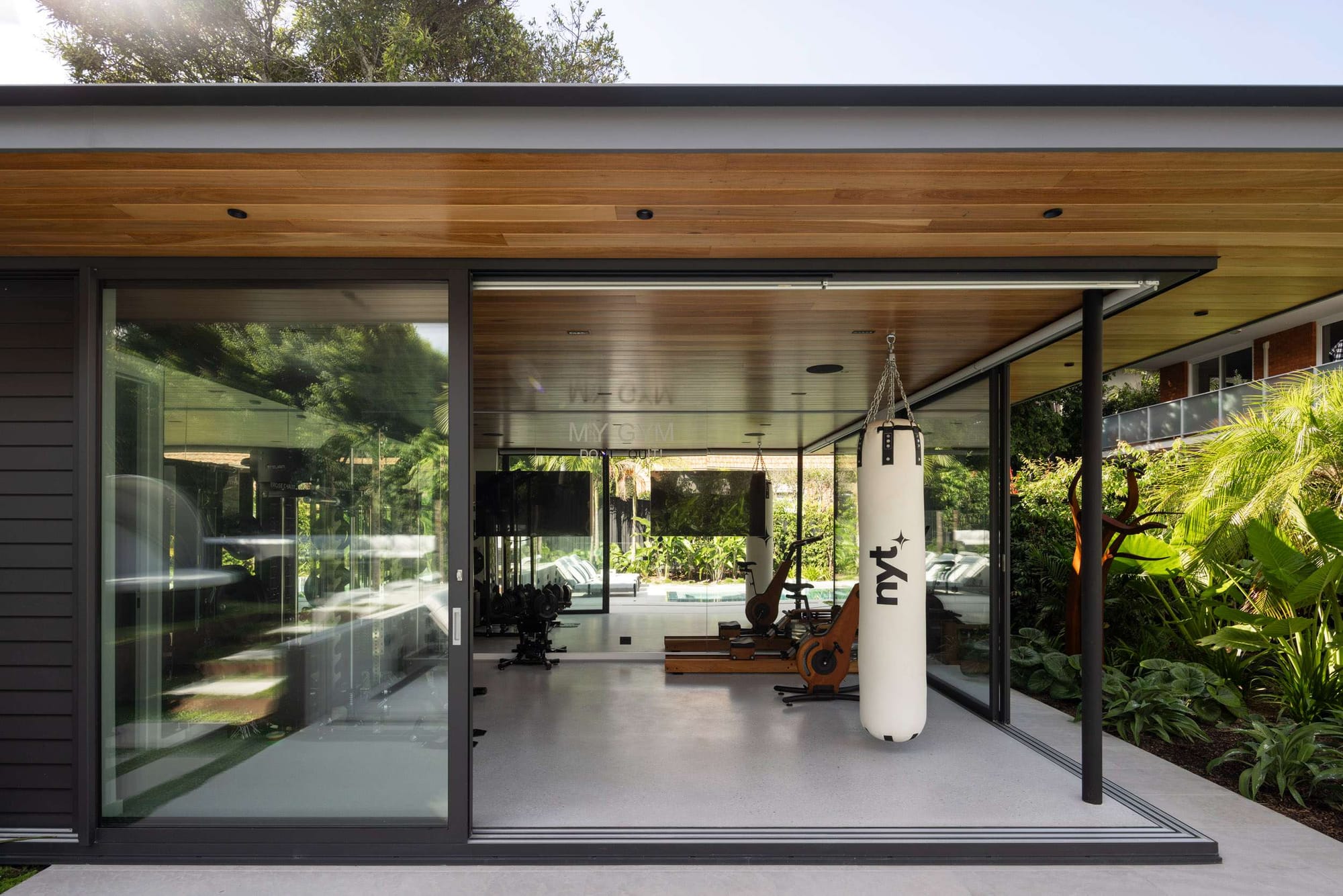 Timber-clad extension with an angled skillion roof and glass sliding doors opening to a garden courtyard with outdoor seating, by Leanhaus.