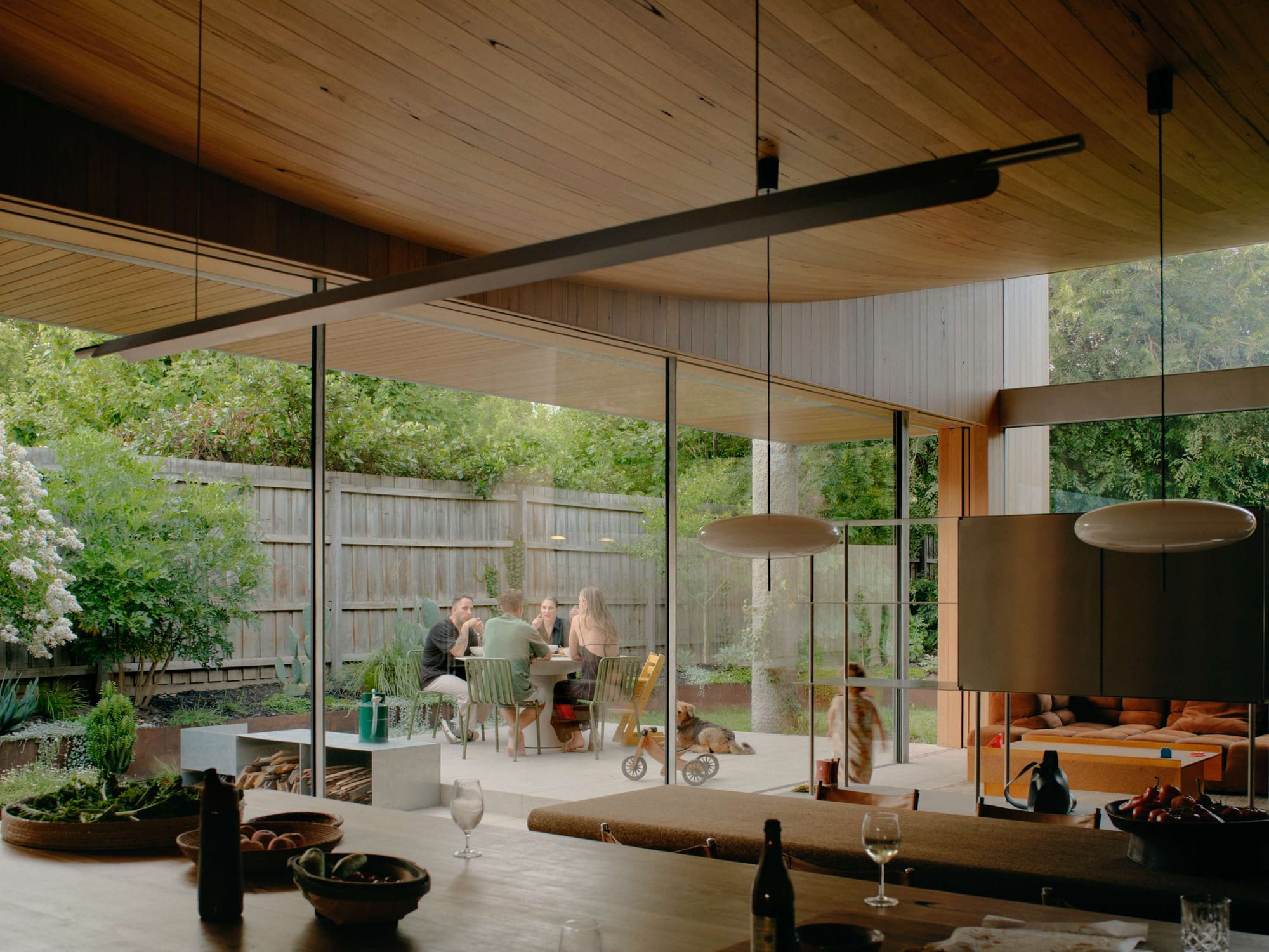 Open-plan kitchen and dining pavilion with a curved timber ceiling and full-height glass doors leading to an outdoor dining area, by Cera Stribley.