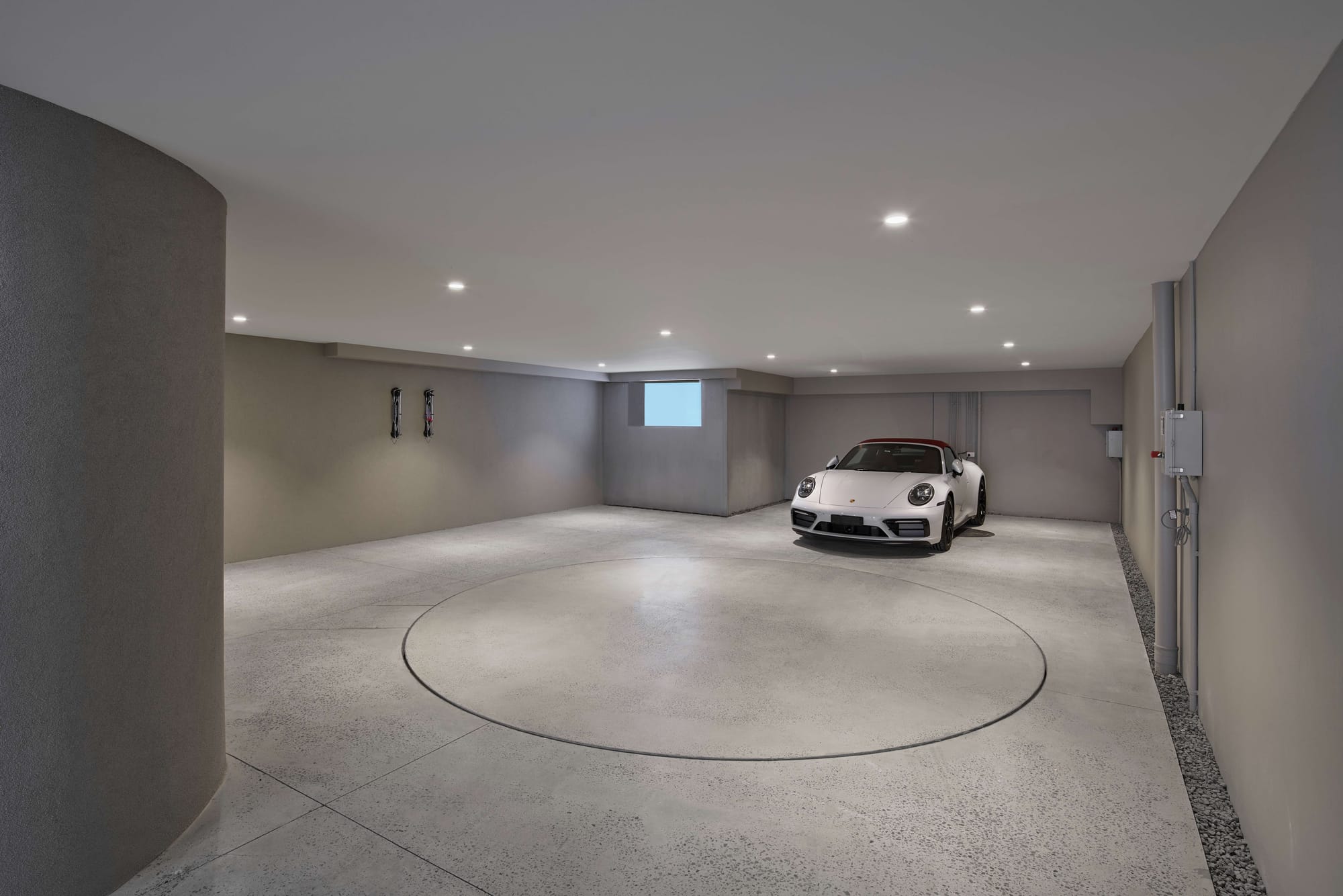 Spacious garage with grey walls, recessed ceiling lights, a circular vehicle turntable and a white sports car.