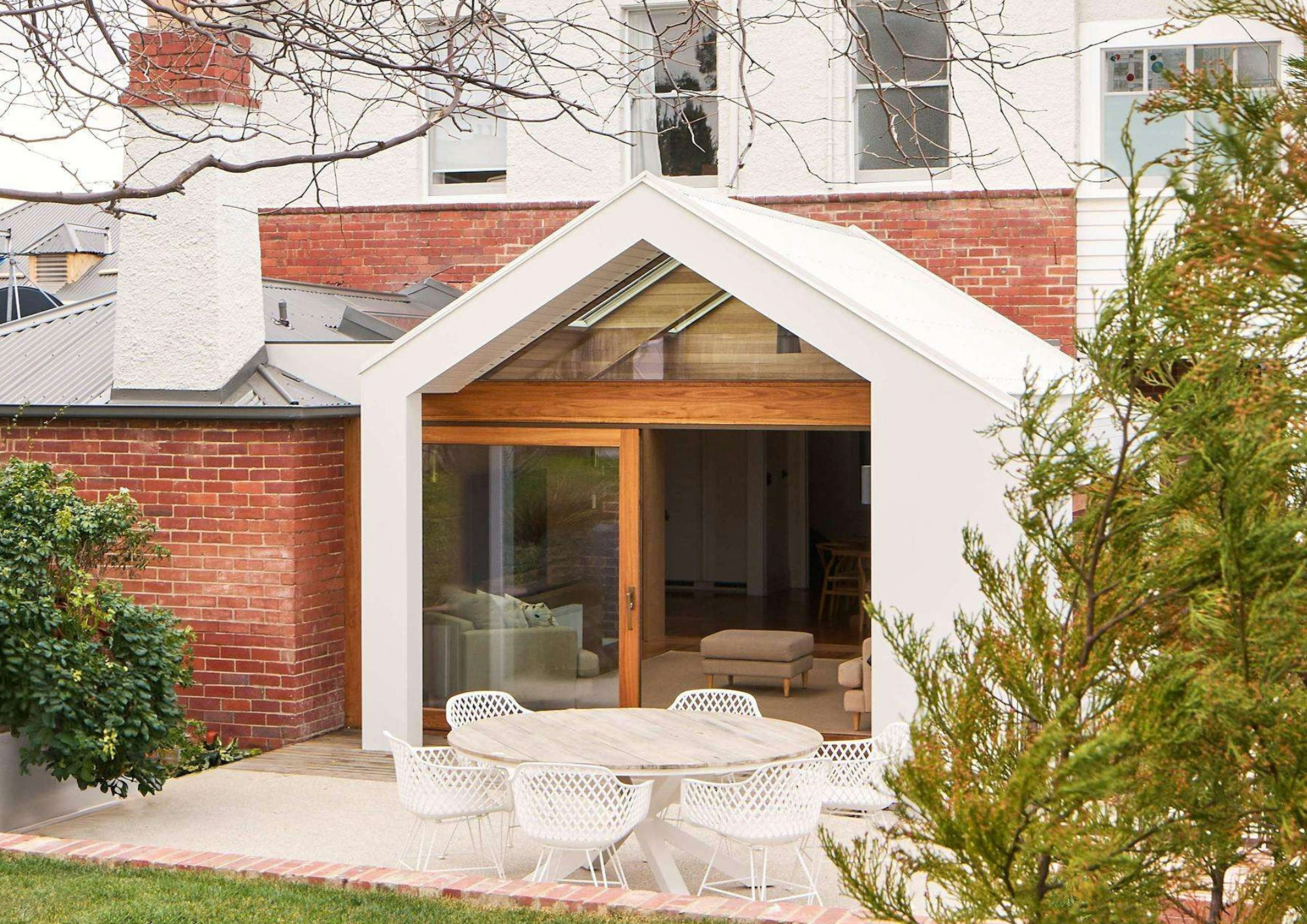 Garden view of Laroona by Biotope Architecture and Interiors, showing a white pitched roof sunroom with timber framed glazing beside original red brick walls.