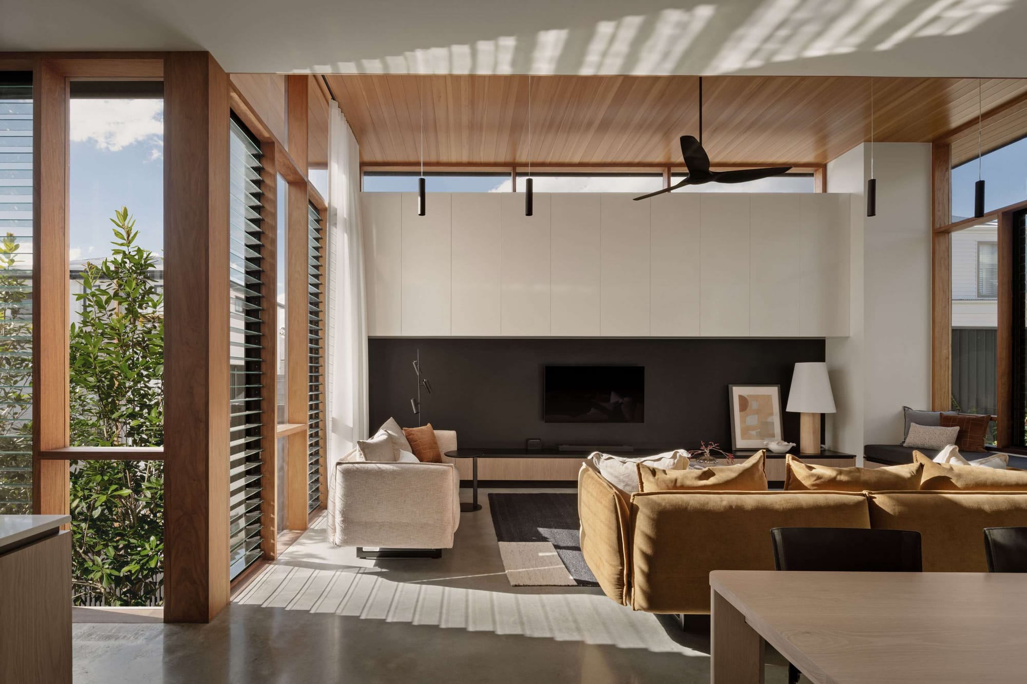 Sunlight filters through tall louvre windows onto concrete flooring beneath a timber ceiling at Light Pavilion House by FOLAR Architecture & Interiors.