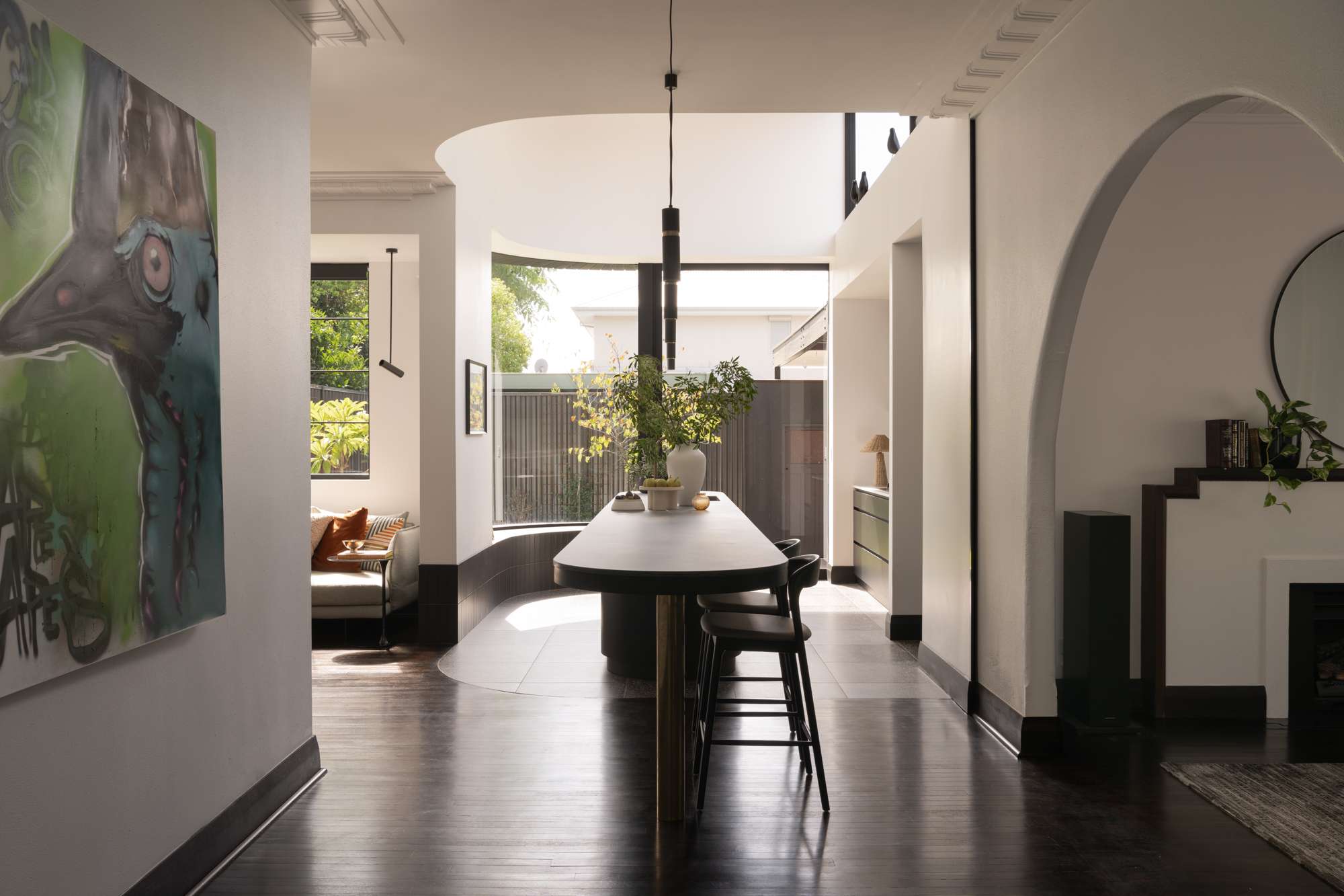 Light-filled dining area with dark timber floors, curved openings, contemporary artwork and views of the garden.
