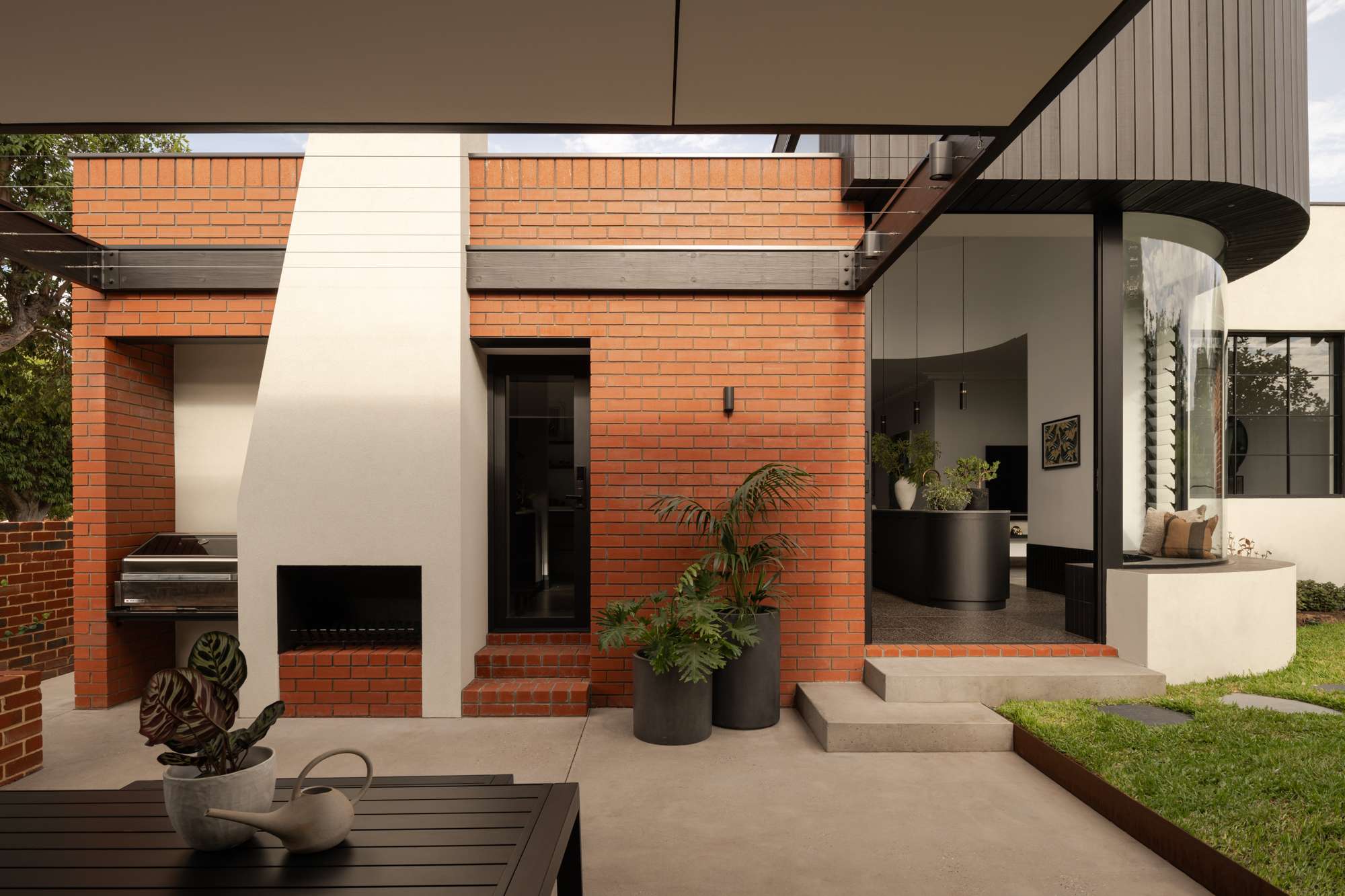 Contemporary brick home extension with a curved glass window, outdoor fireplace and landscaped courtyard.