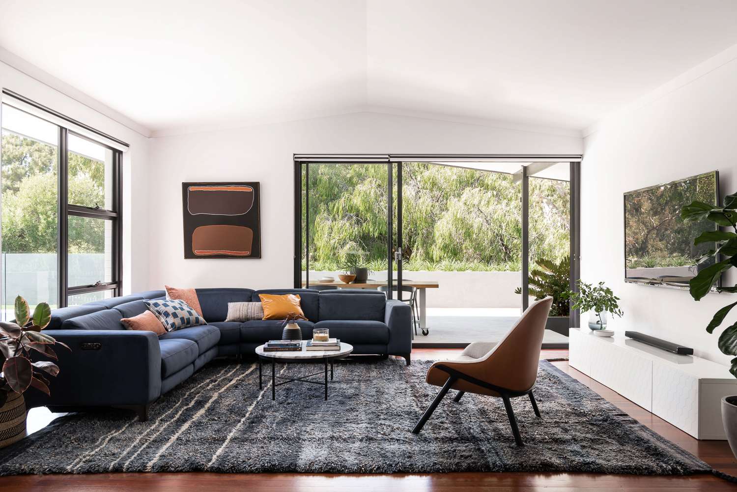 Bright living room with a navy sectional sofa and large sliding doors opening to a leafy terrace.