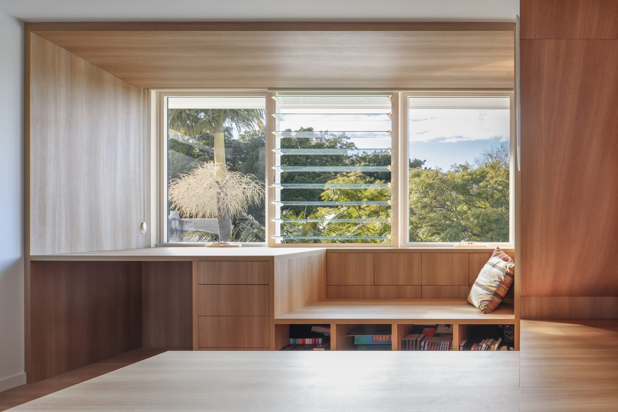 Timber-lined study nook with integrated desk, window seat and shelving overlooking leafy treetops.
