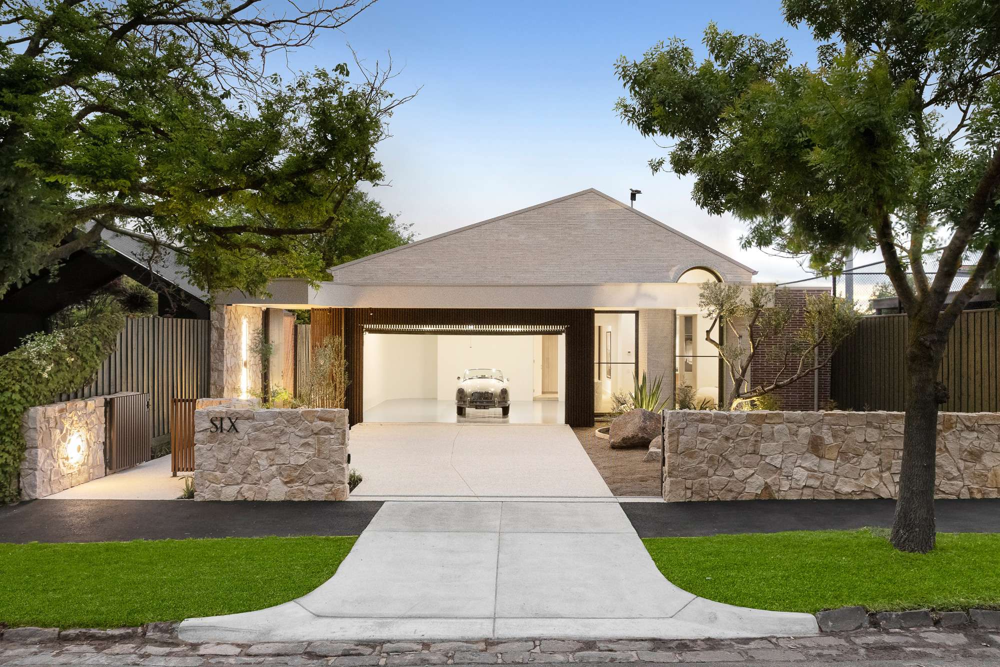 Contemporary brick home with an open garage, vintage car, timber screening and a low stone boundary wall.