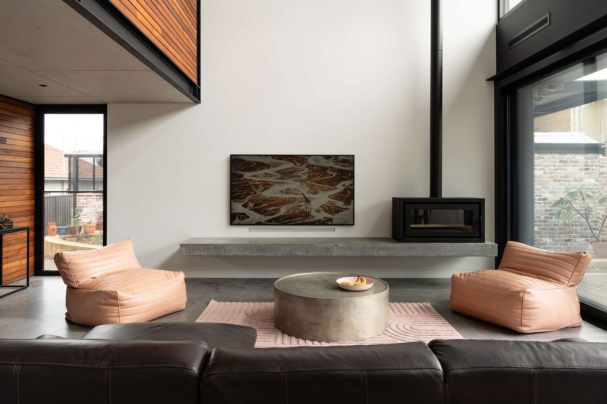 Double-height living room with peach armchairs, a round coffee table and a black fireplace above a long concrete hearth.