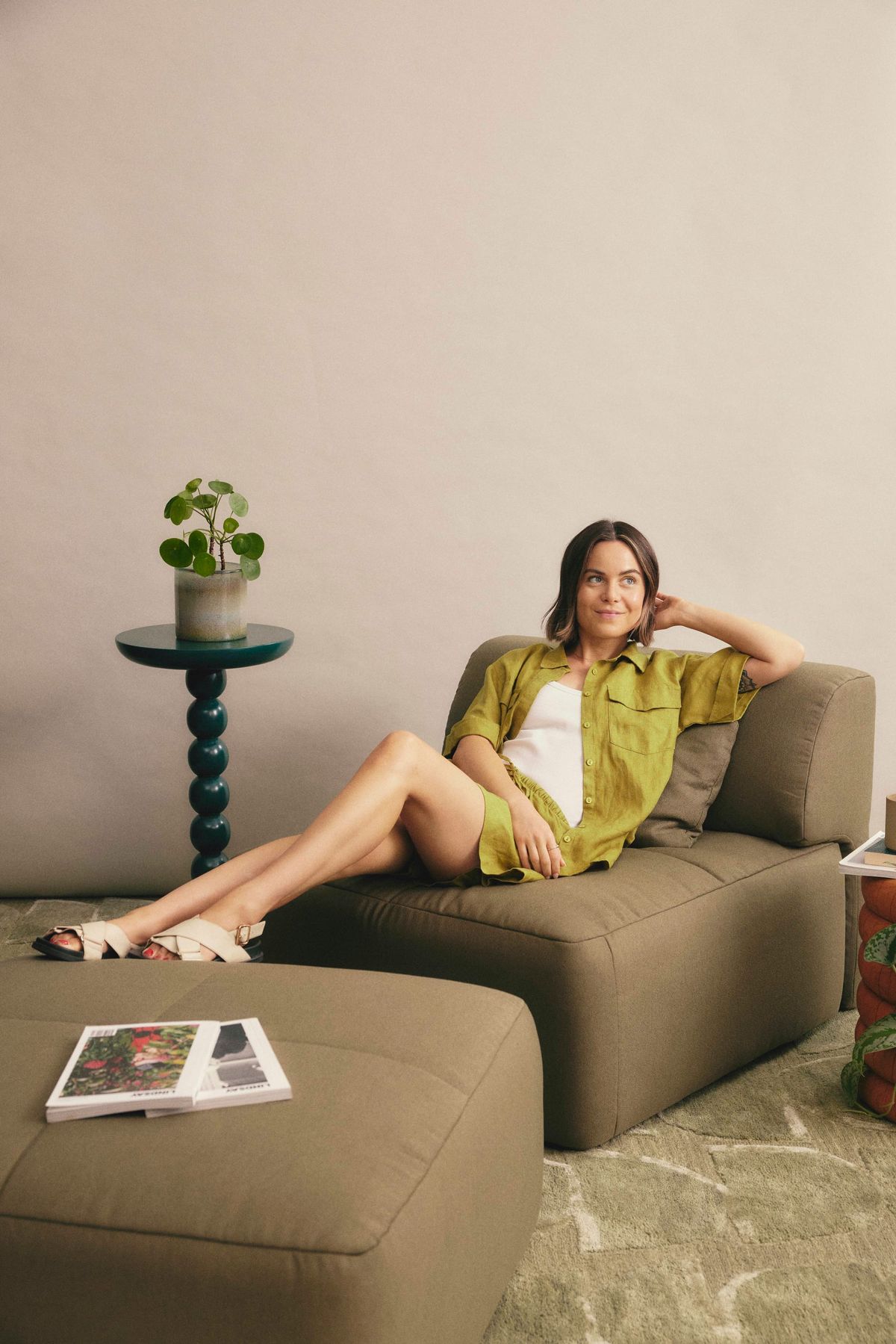 Eva Everyday Sofa. Copyright of Eva. Young woman reclining on olive modular armchair with feet on modular footstool. 