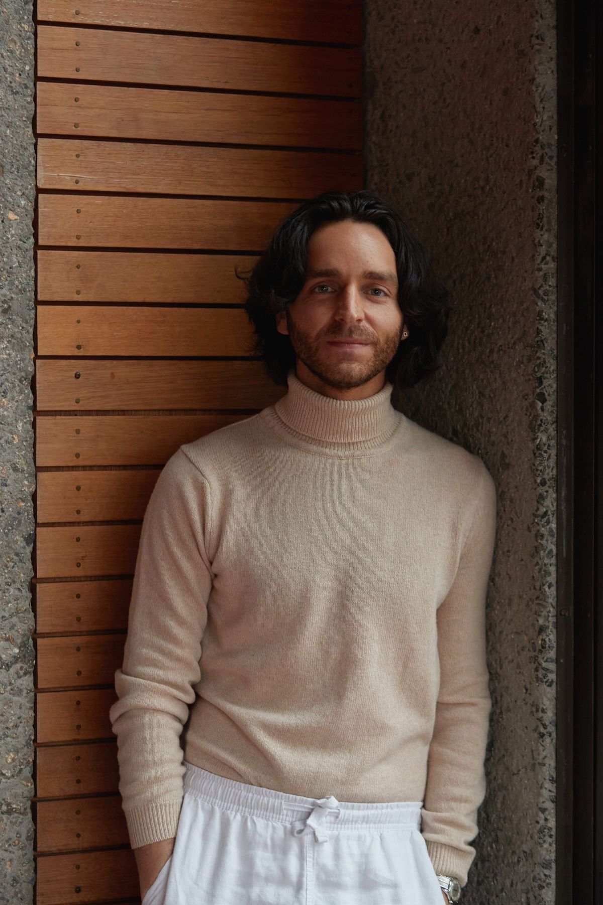Benjamin Shand of Studio Shand. Photograohy by Traianos Pakioufakis. Headshot of man with beige jumper and long dark hair. 