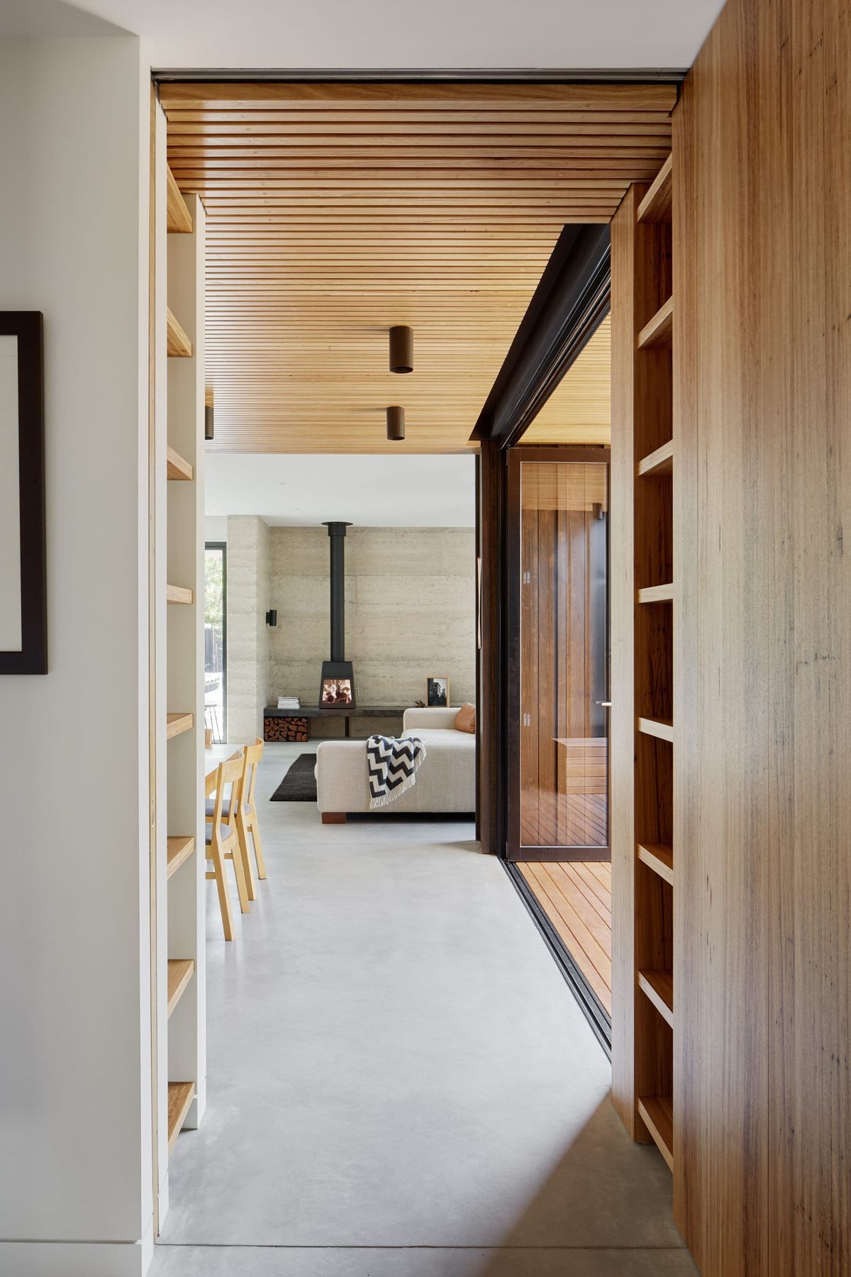 Polished concrete floor in open plan living and dining room and hallway. Rammed earth wall behind fireplace in background.