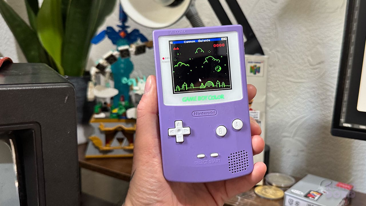 A purple Game Boy Color showing a game called Cannon Defense