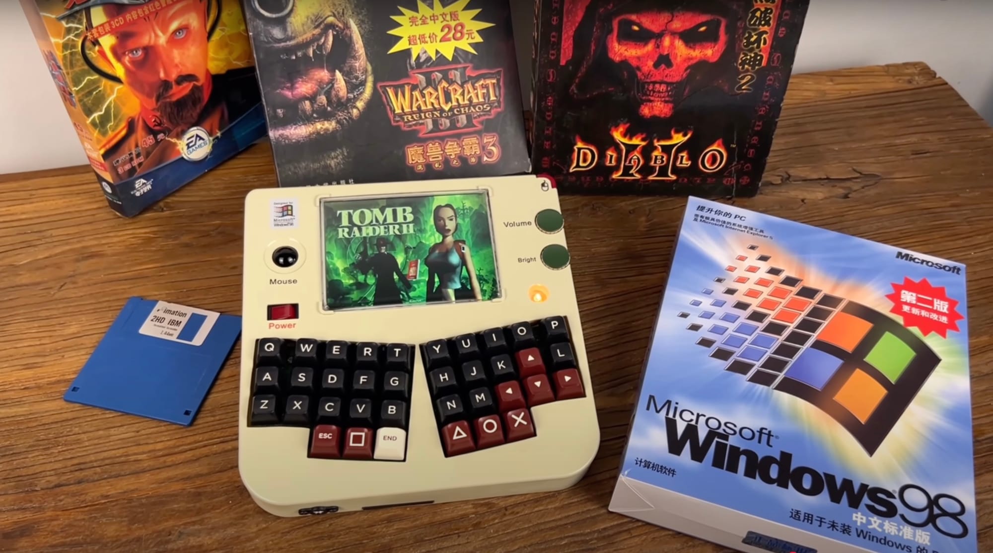 Tomb Raider loading screen on a custom retro handheld with a full sized keyboard. There are game boxes scattered around it.