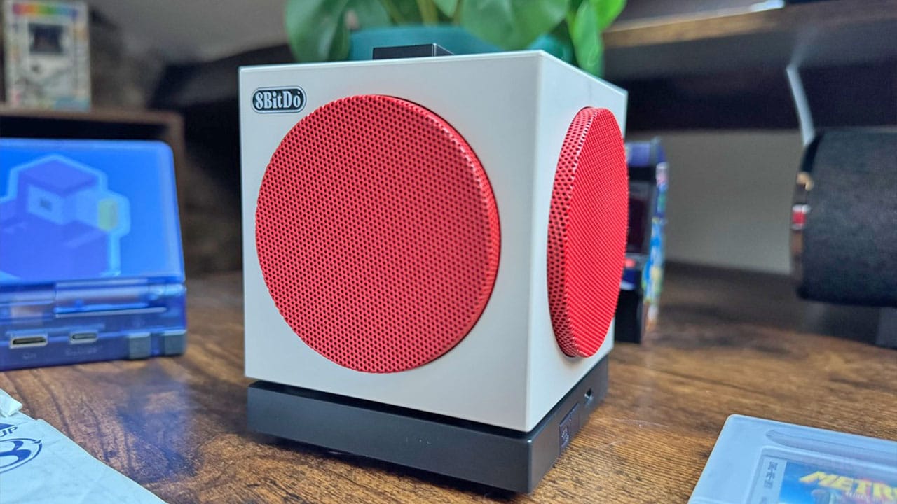 A grey speaker shaped like a cube with red speaker grills that look like buttons