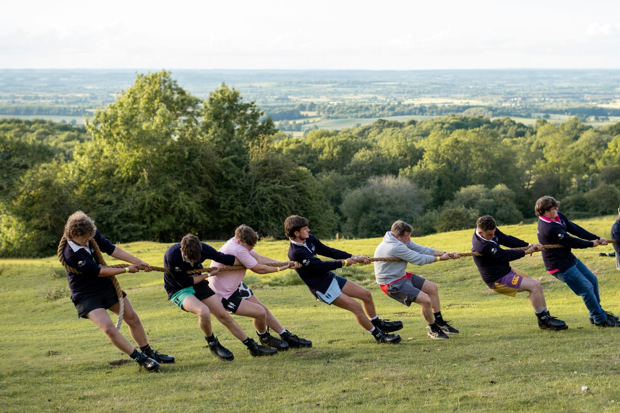 People are playing tug-of-war on a grassy hillside.