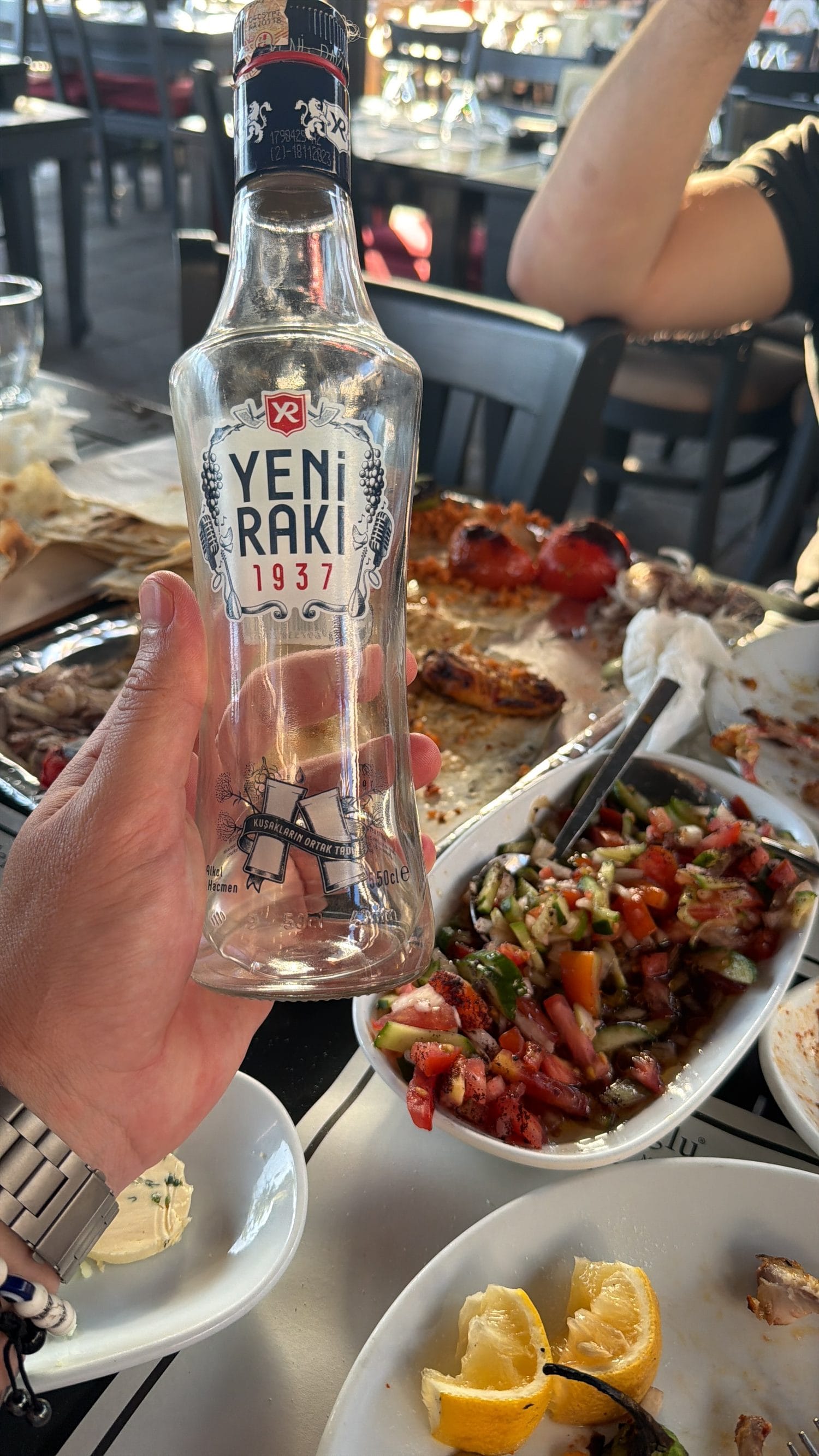 A bottle of Yeni Rakı and a glass held over a table of Turkish meze