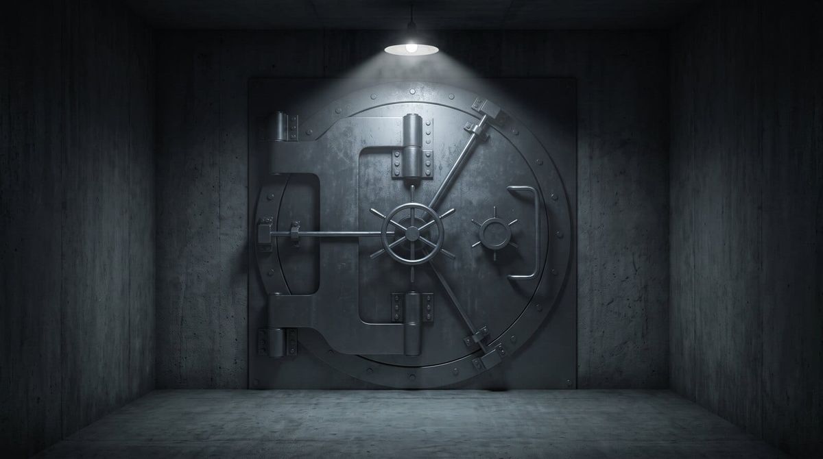 A massive sealed steel vault door in a windowless concrete chamber under one hard cone of overhead light.