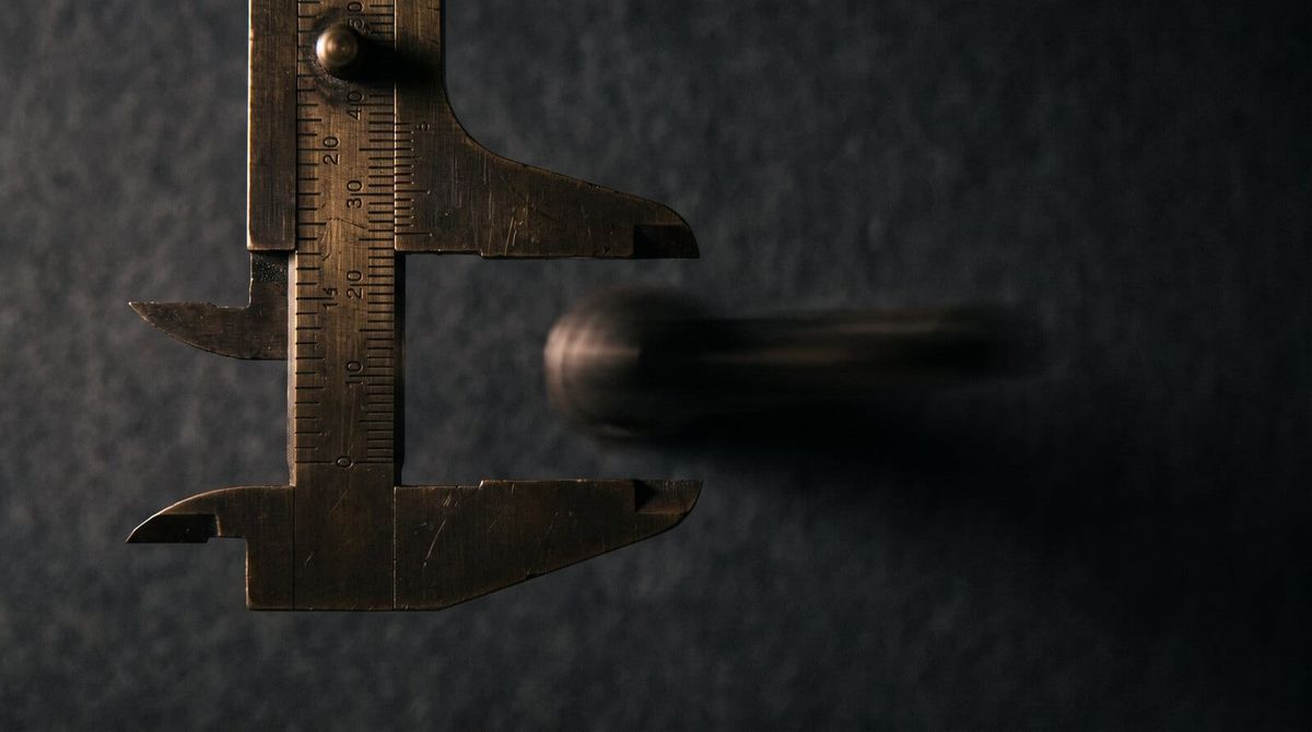 A brass vernier caliper open on an object streaking out of its jaws in motion blur, dissolving into darkness.