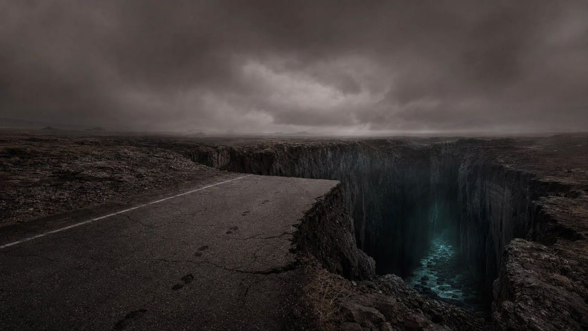 A cracked road ends at the edge of a widening chasm under a heavy overcast sky, ghosted footprints slowing to a stop before the void.