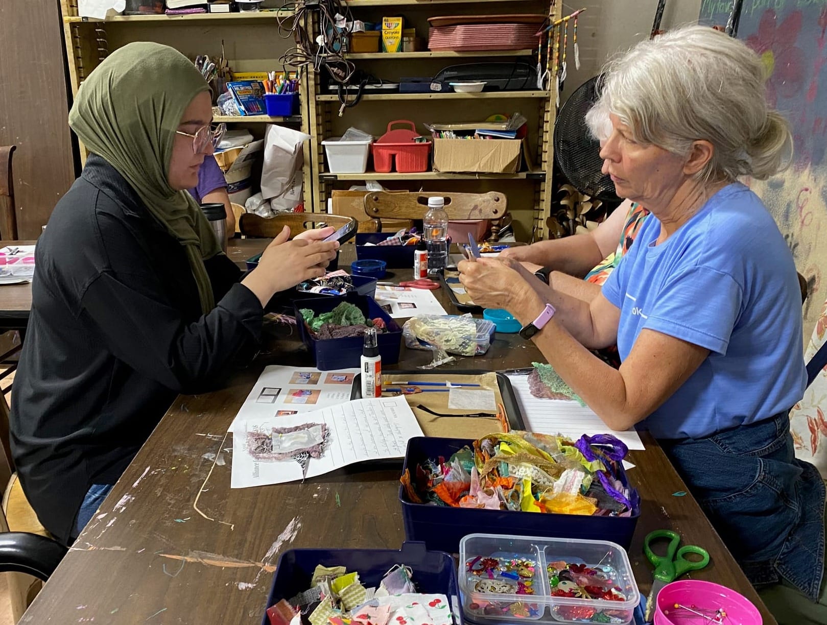 Several female-presenting people hunch over art supplies and work on art projects.