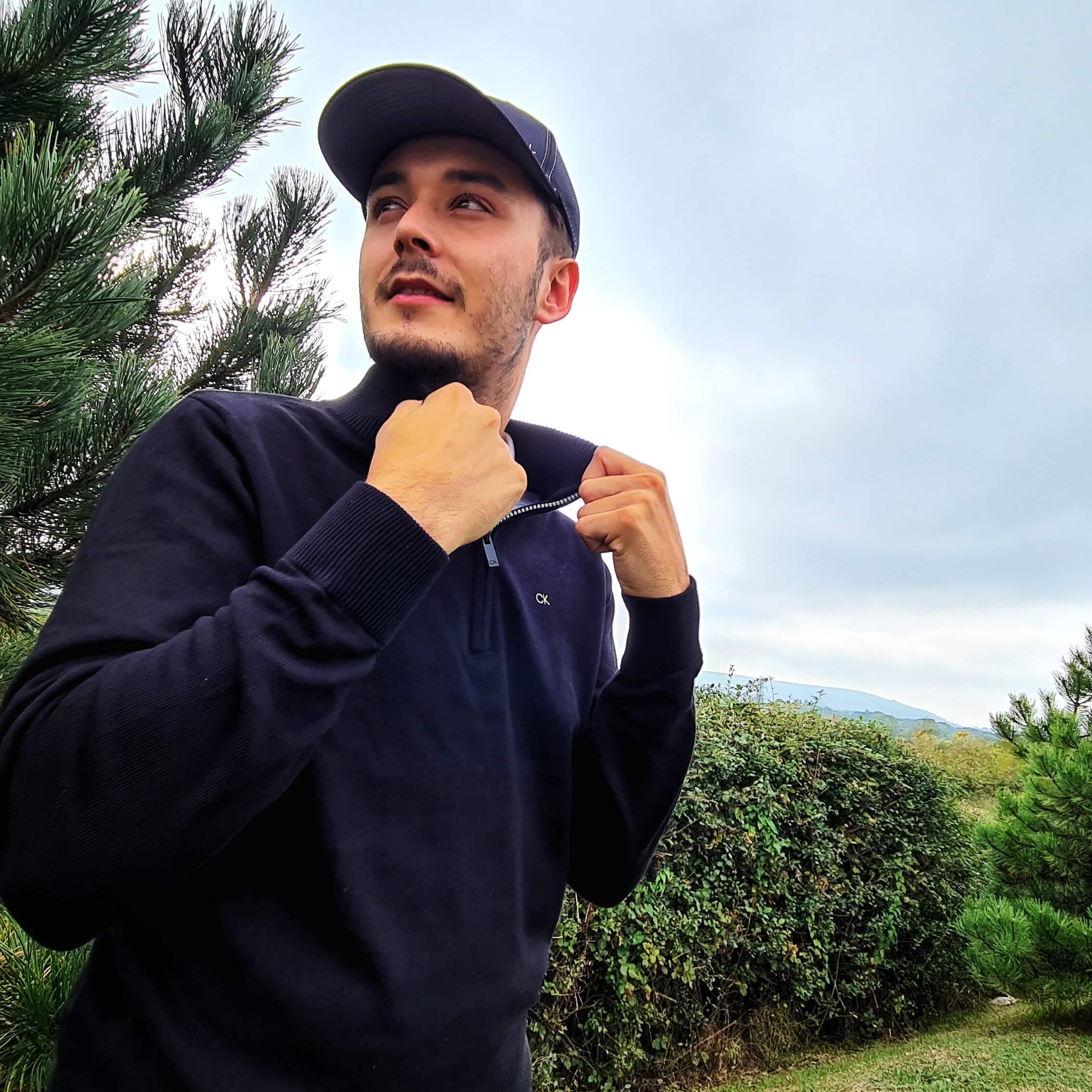 Male golfer wearing a navy Calvin Klein sweater and cap adjusting his collar