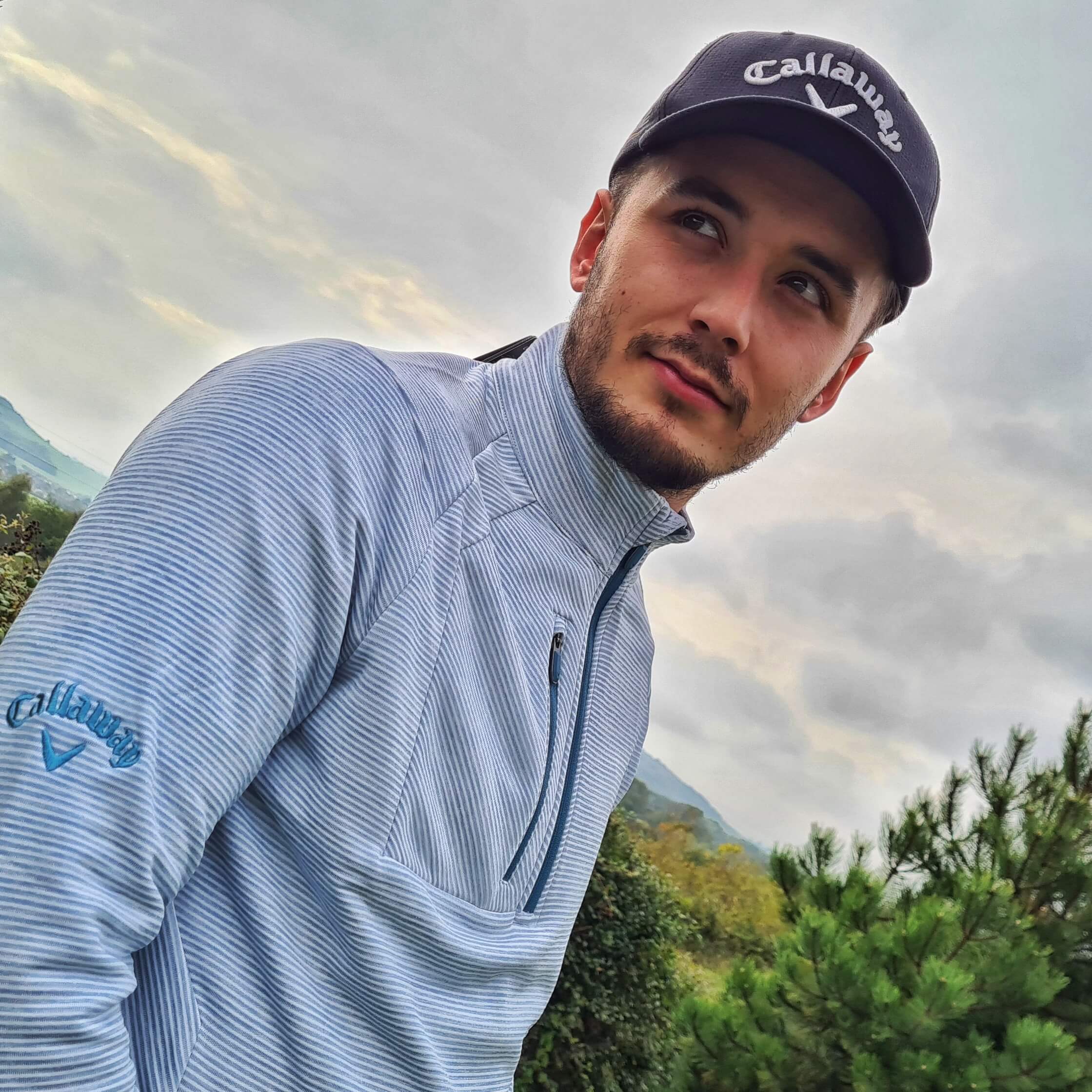 Male golfer wearing a light blue midlayer with the Callaway logo on his arm and cap
