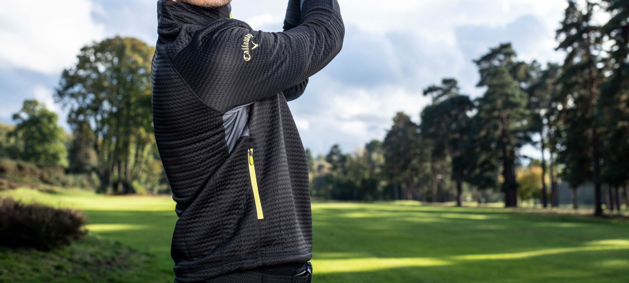 Male golfer on a fairway wearing a golf sweater and swinging a golf club