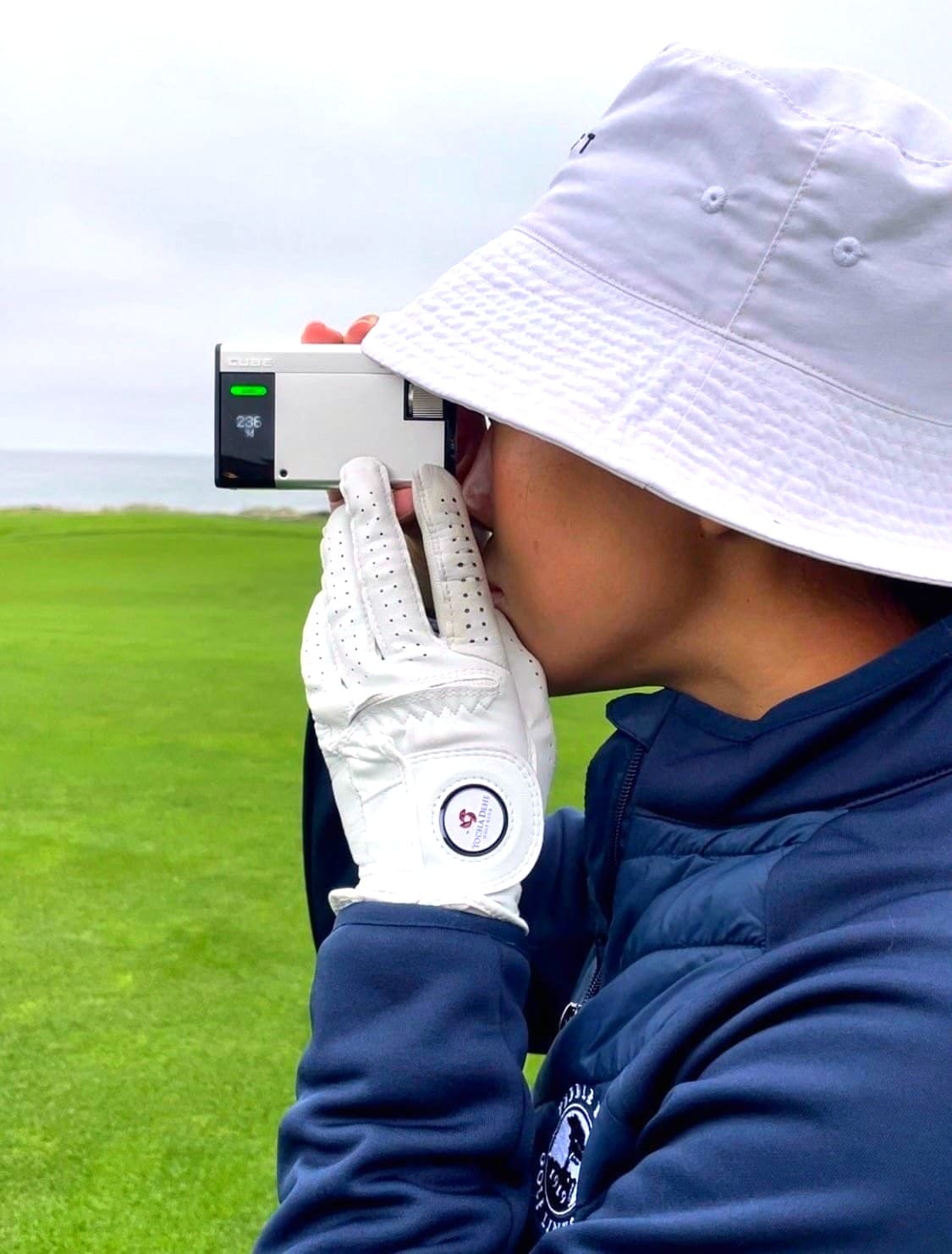 A golfer looks through the CUBE on a golf course.  A golf glove with ball marker is centre frame.