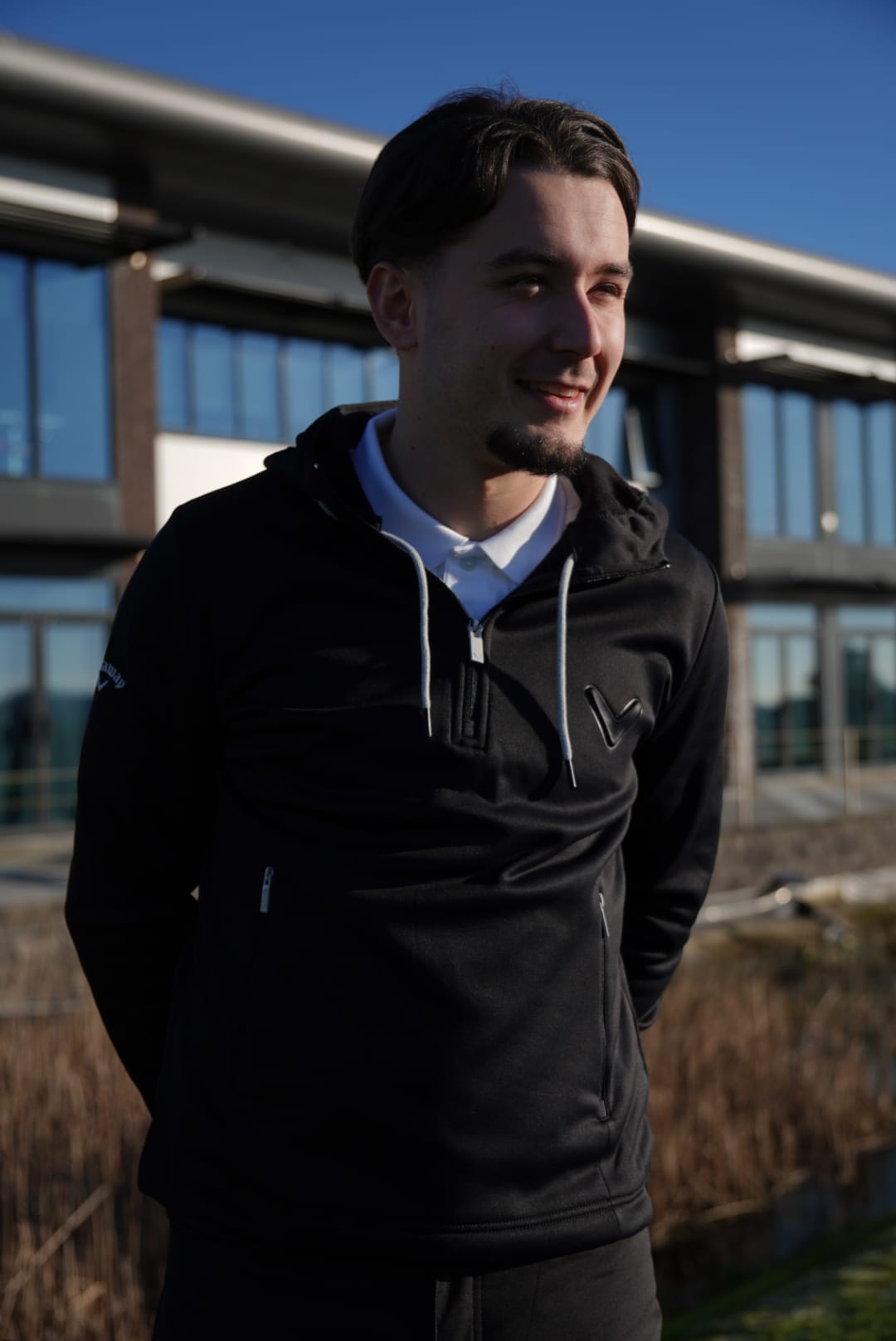 Man wearing the Callaway Thermal Hoody in front of a large modern clubhouse