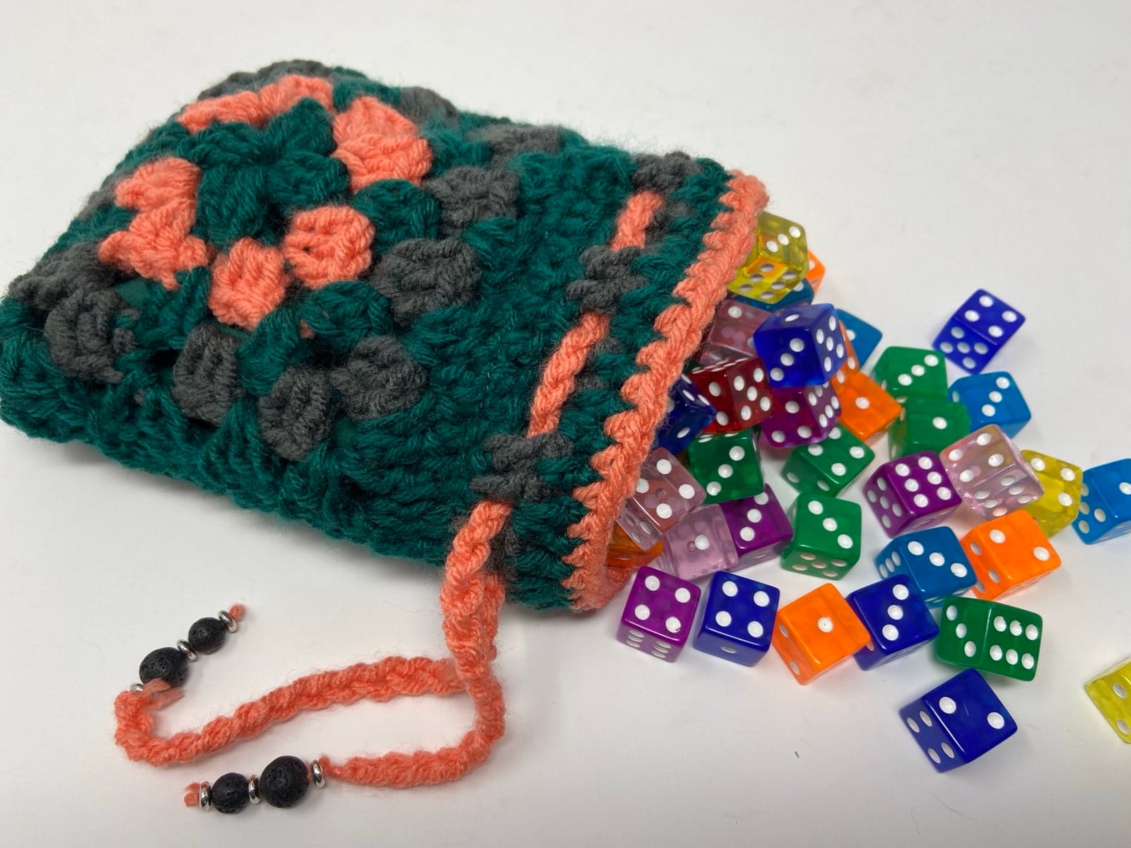 Teal, coral, and gray crocheted dice bag with colorful dice spilling out.