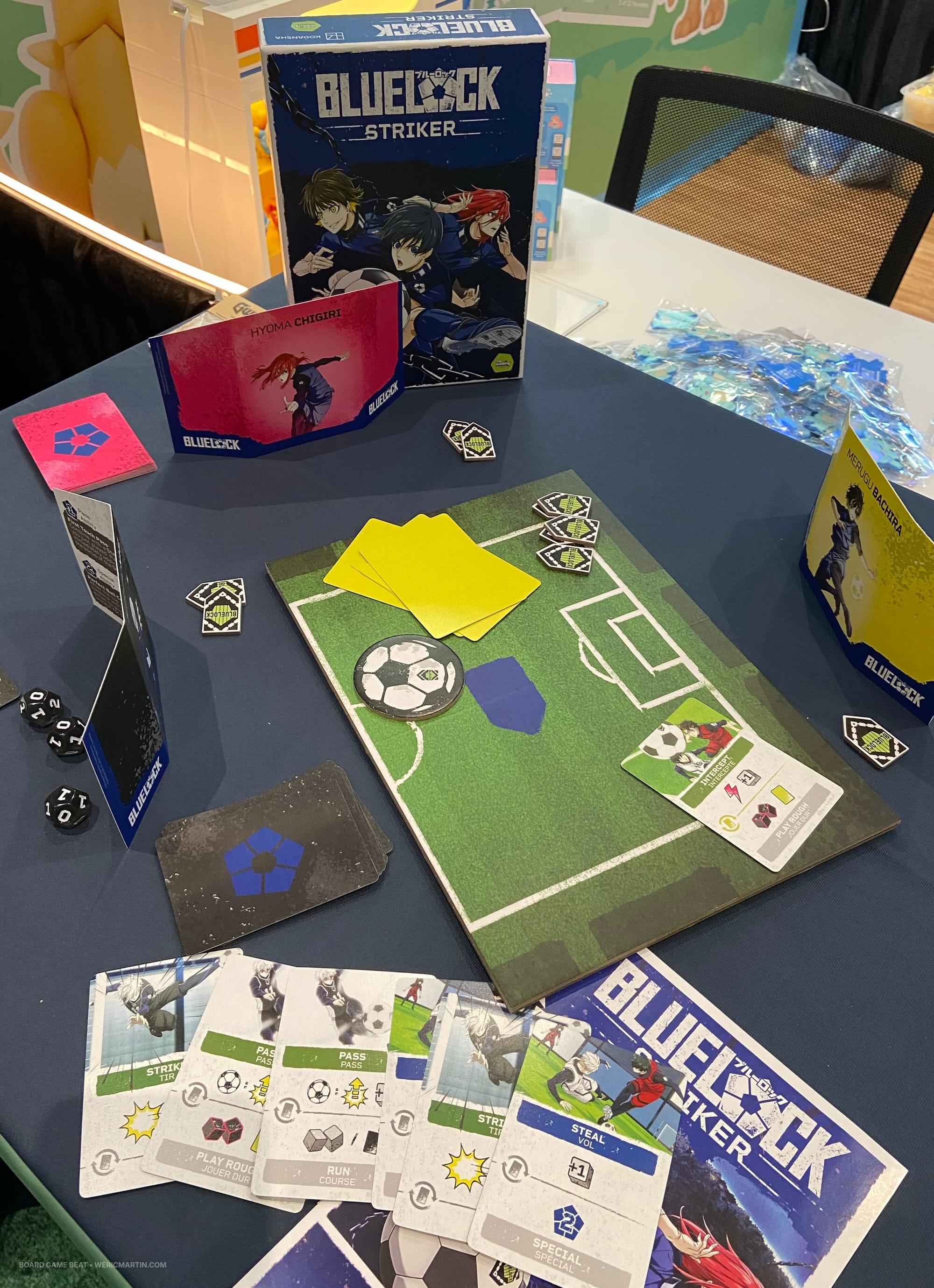 Components for Blue Lock Striker: cards showing soccer moves, dice, and a tiny game board featuring half of a soccer field