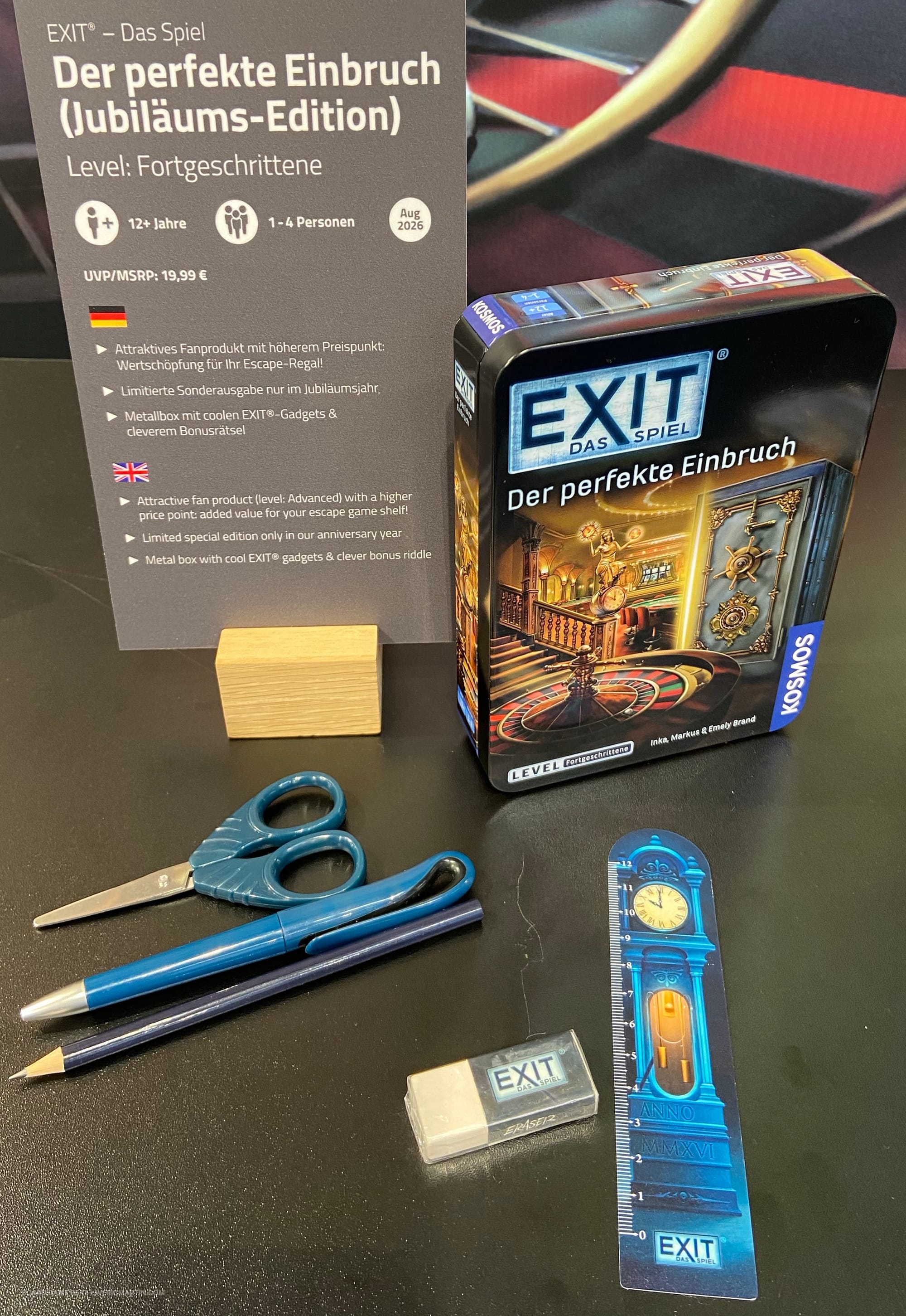 The metal box for EXIT: Das Spiel - Der perfekte Einbruch is on display, along with scissors, a pen, a pencil, an eraser, and a branded ruler