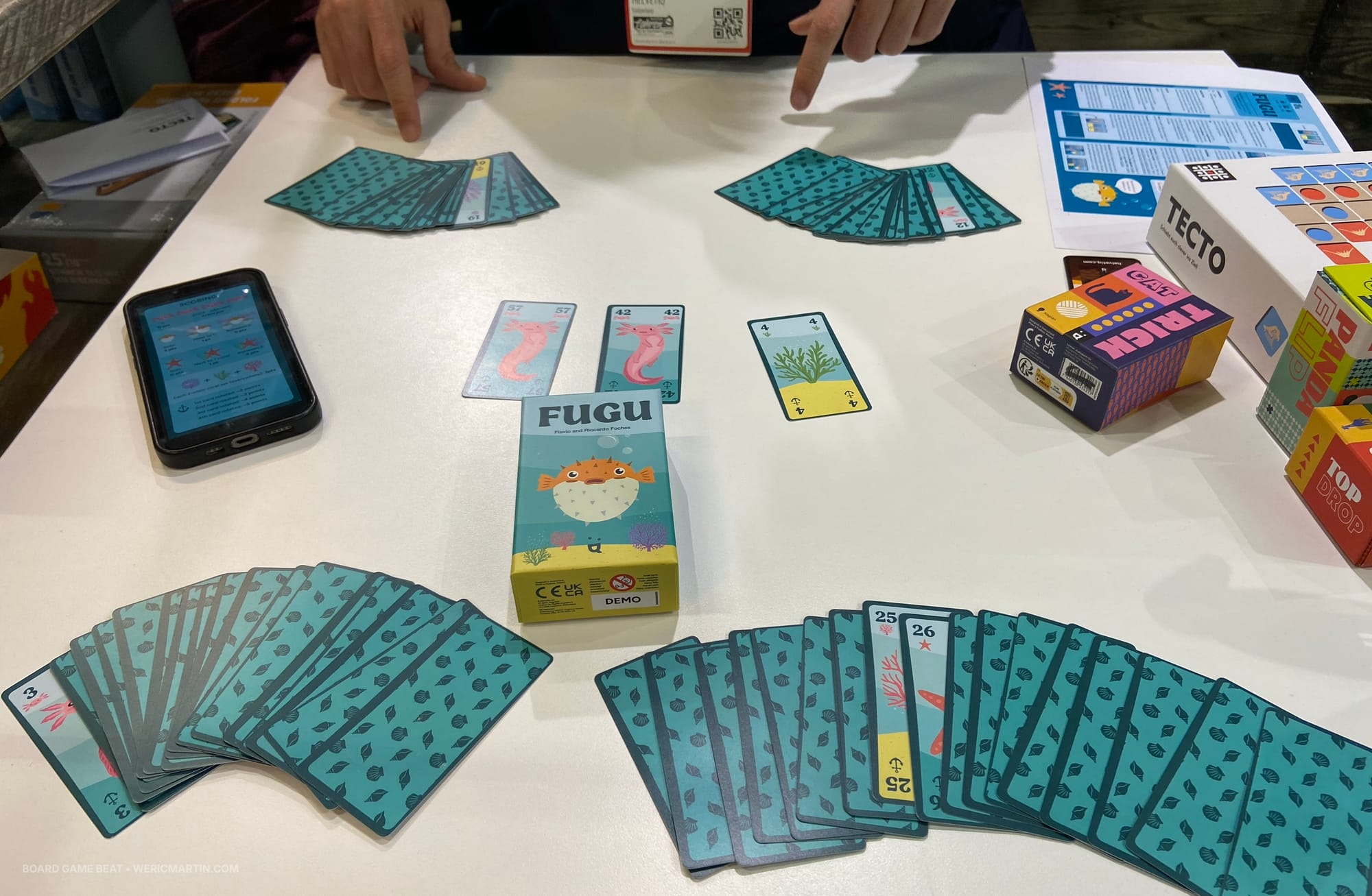 Four hands of cards on the table, with most cards being face down; three cards are face up in a market