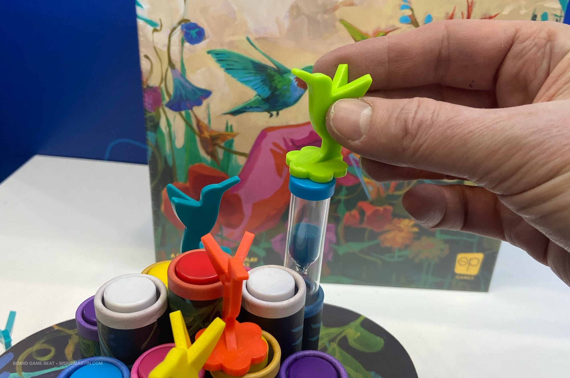 A hand holds a green plastic hummingbird, which is magnetized and has a sand timer stuck to its base