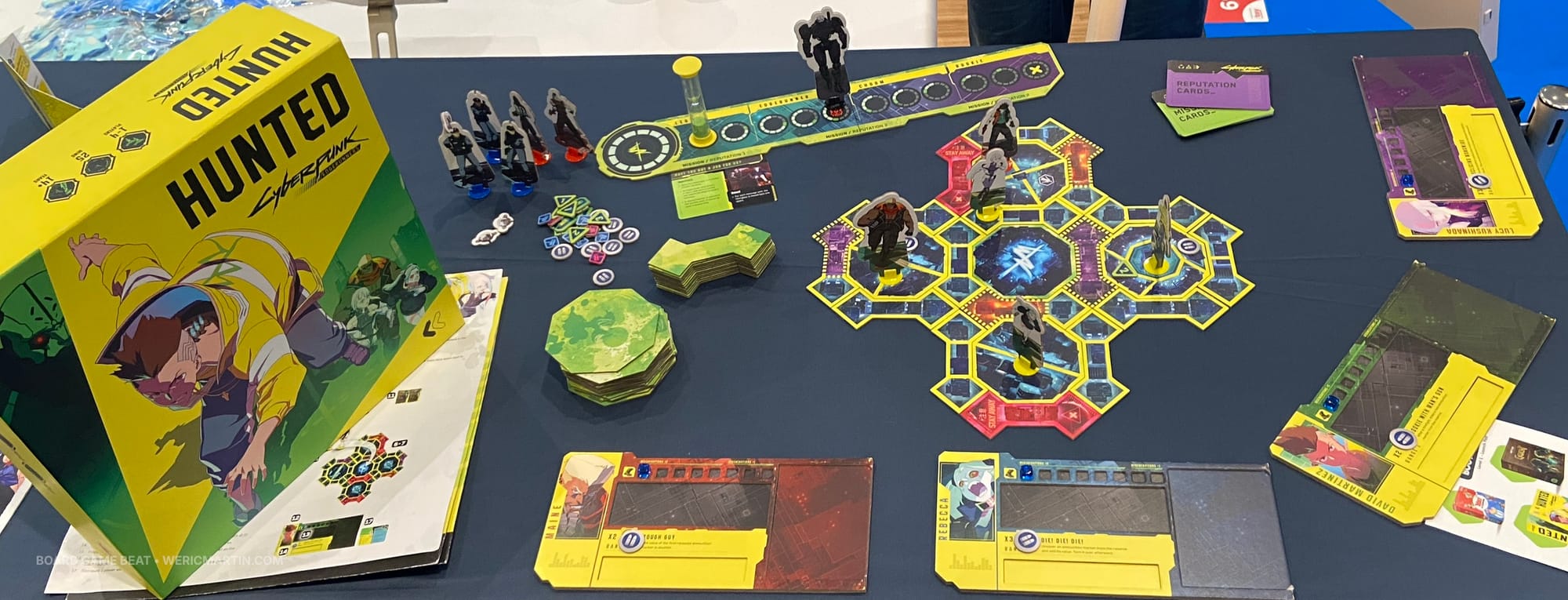 All of the components of Cyberpunk Edgerunners: Hunted, including player boards, stacks of tiles, a dozen standees, and tokens