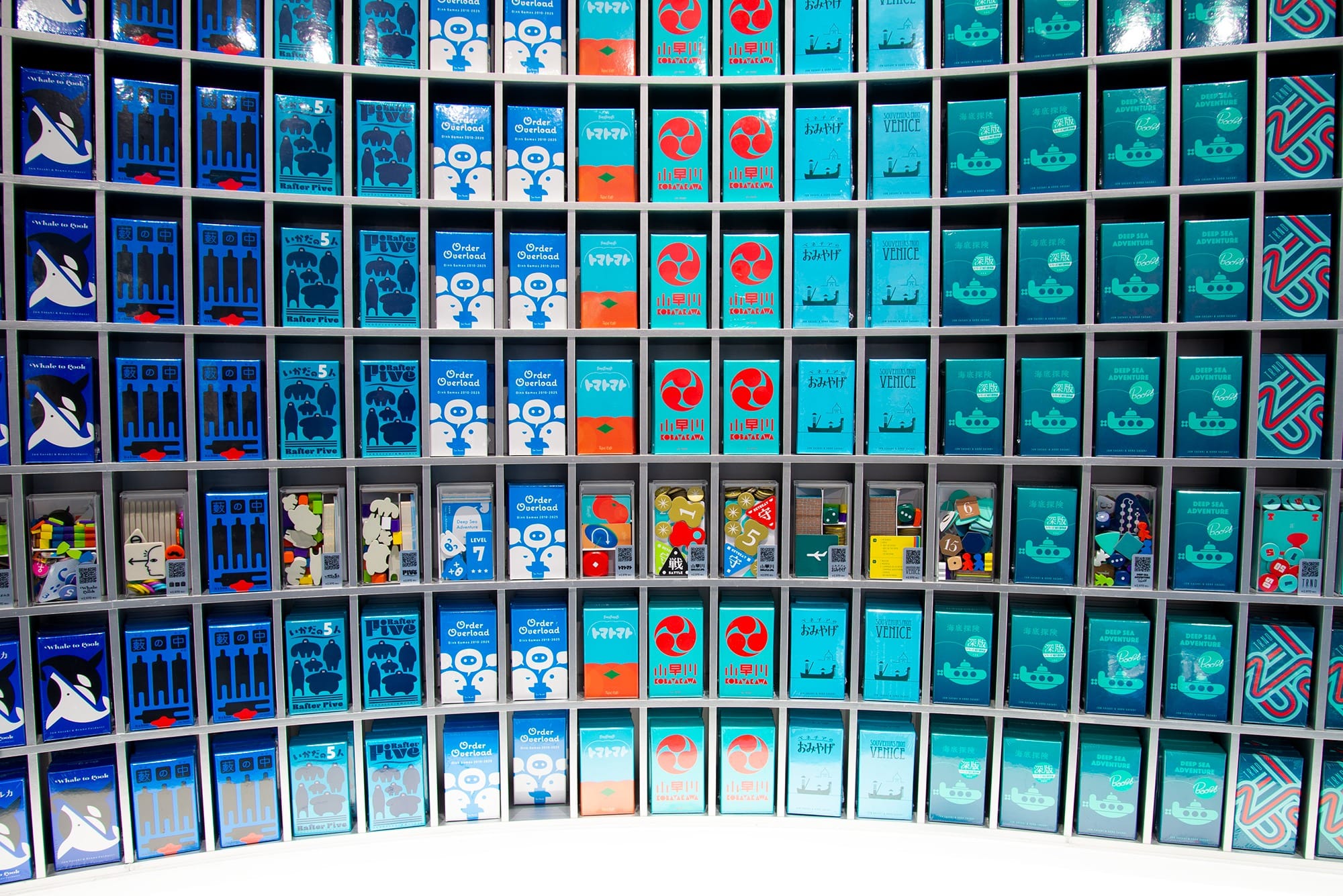 Depicted: A close-up of the shelves at the Oink Games store, showing a row pf plastic cases that display the pieces inside the box in that column