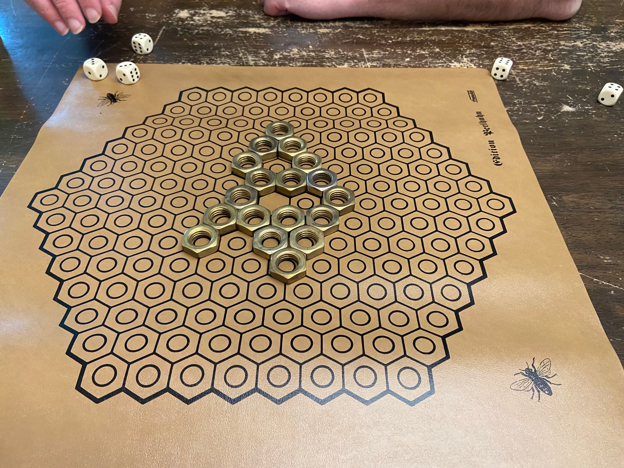 Five dice stand near a hexagonal gameboard that has 18 metal nuts on it