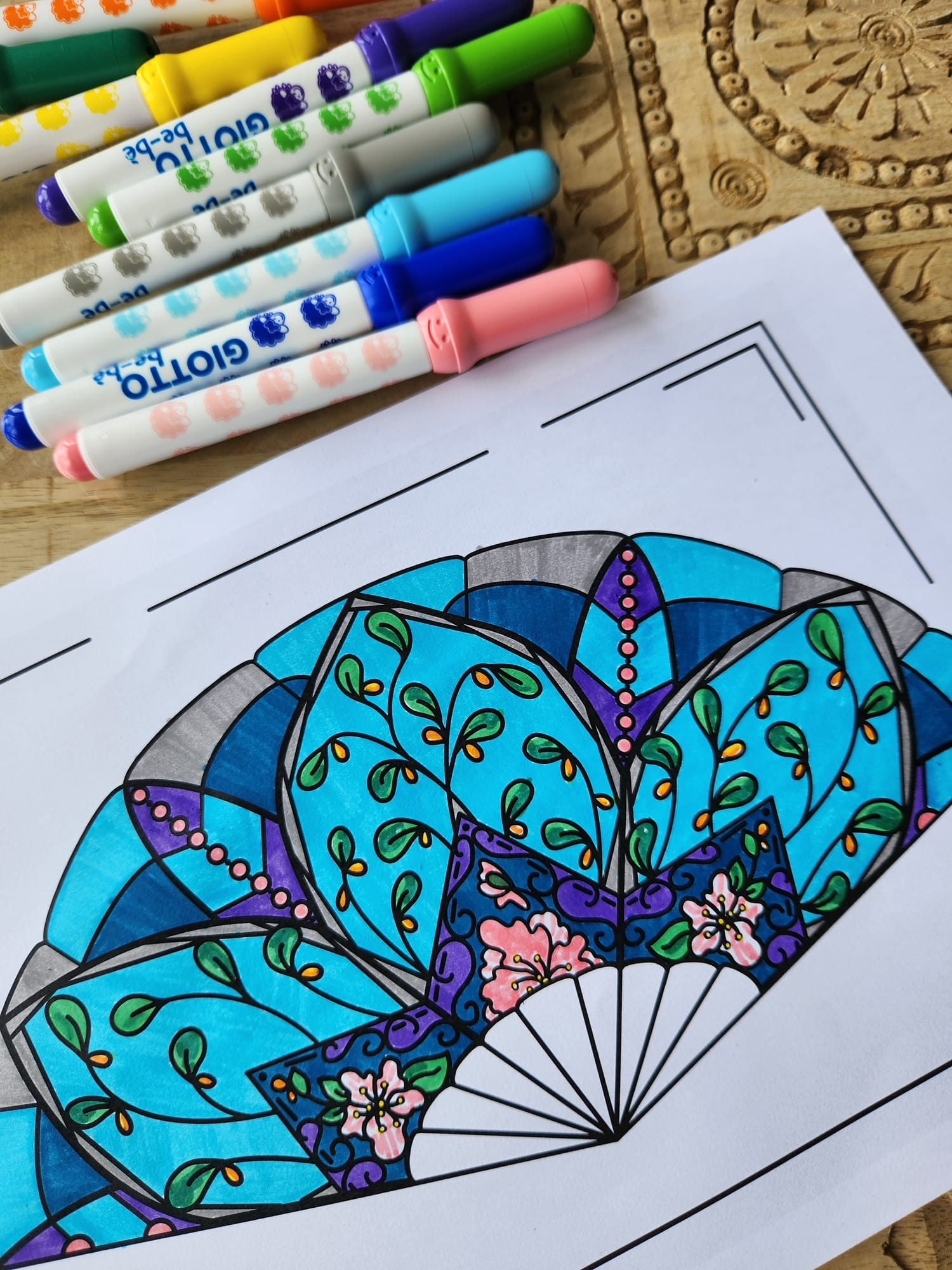 A black-and-white illustration of a fan has been colored with markers, which are included in this image