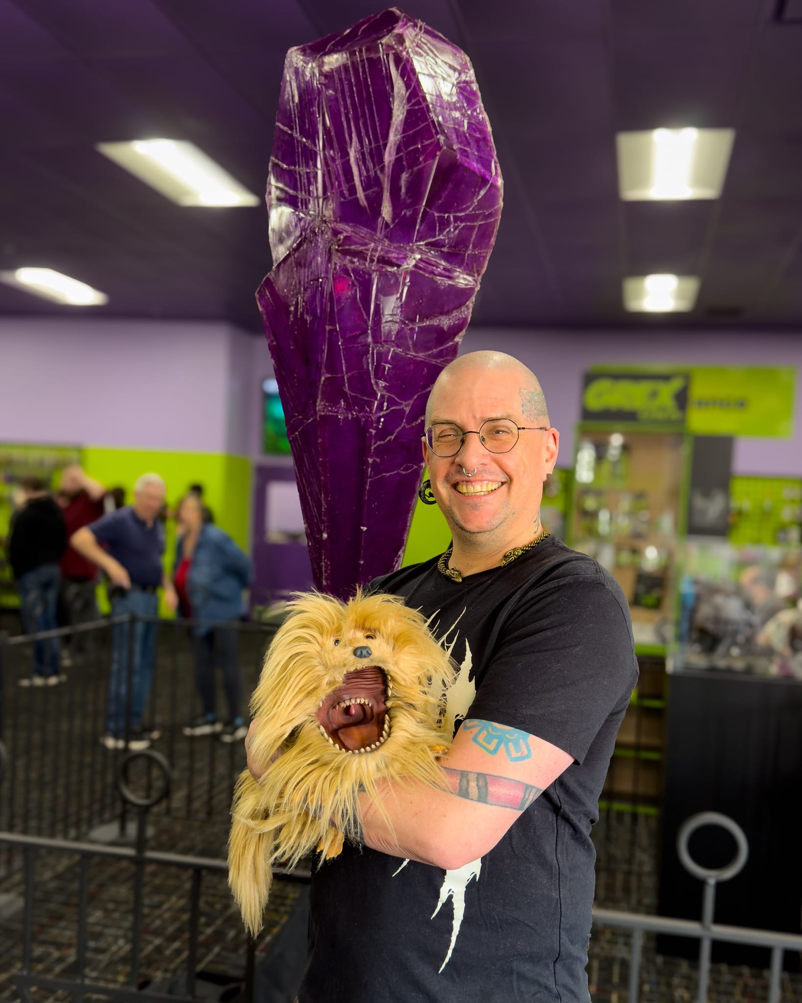 Paul Alexander Butler holds a puppet from The Dark Crystal while standing in front of a four-foot-tall purple crystal