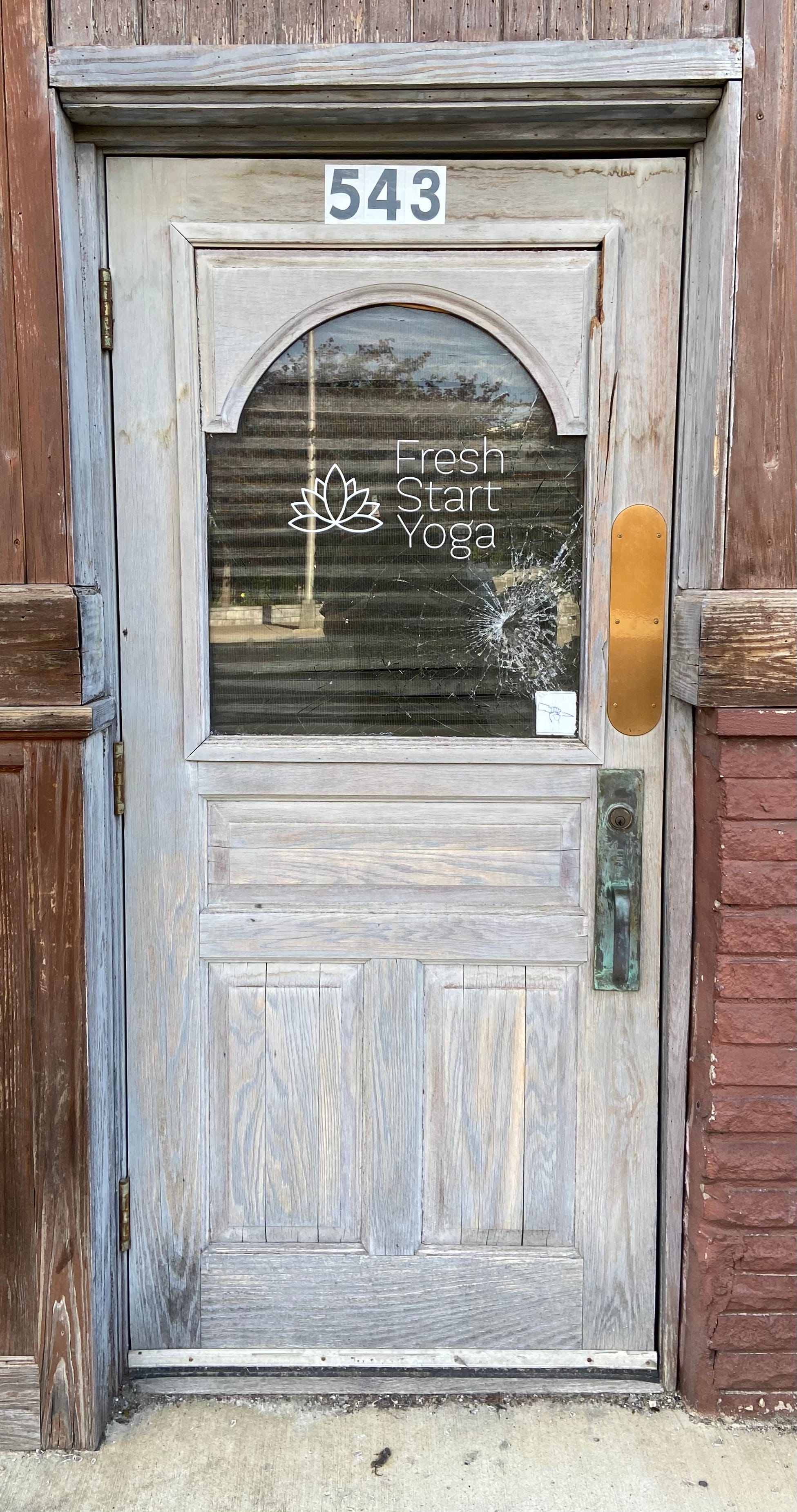 The image shows a wooden door that features a pane of glass shattered in a circular pattern and the words "Fresh Start Yoga"