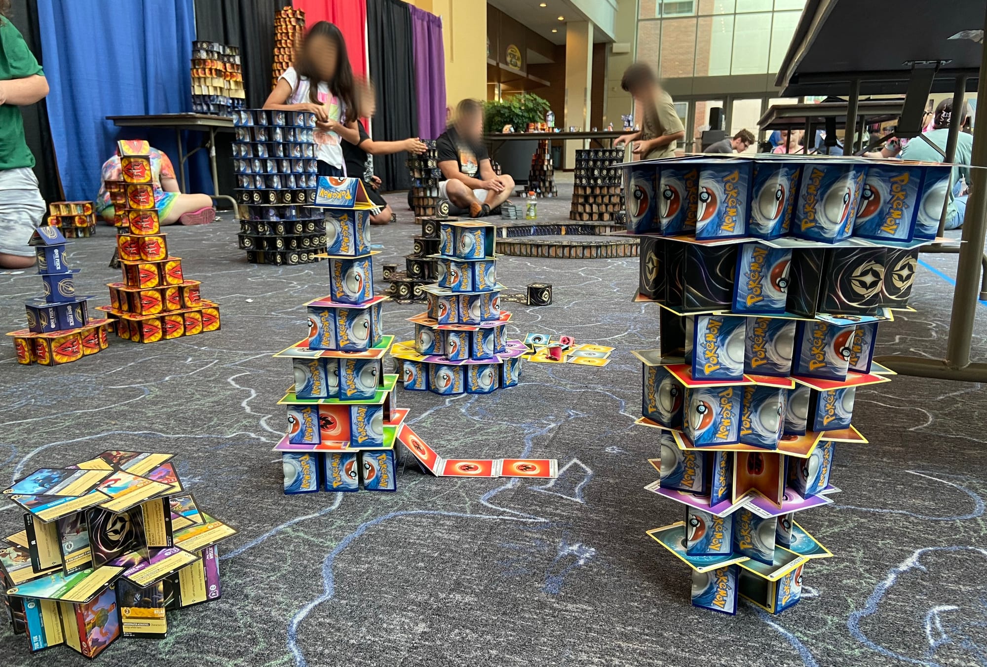 More than a dozen 3D structures created from flat and folded trading cards are built on the carpeted convention floor.