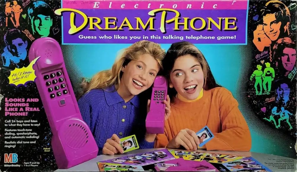 Cover of the 1991 board game Dream Phone, showing two girls listening to a large pink phone surrounded by photos of teenage boys.