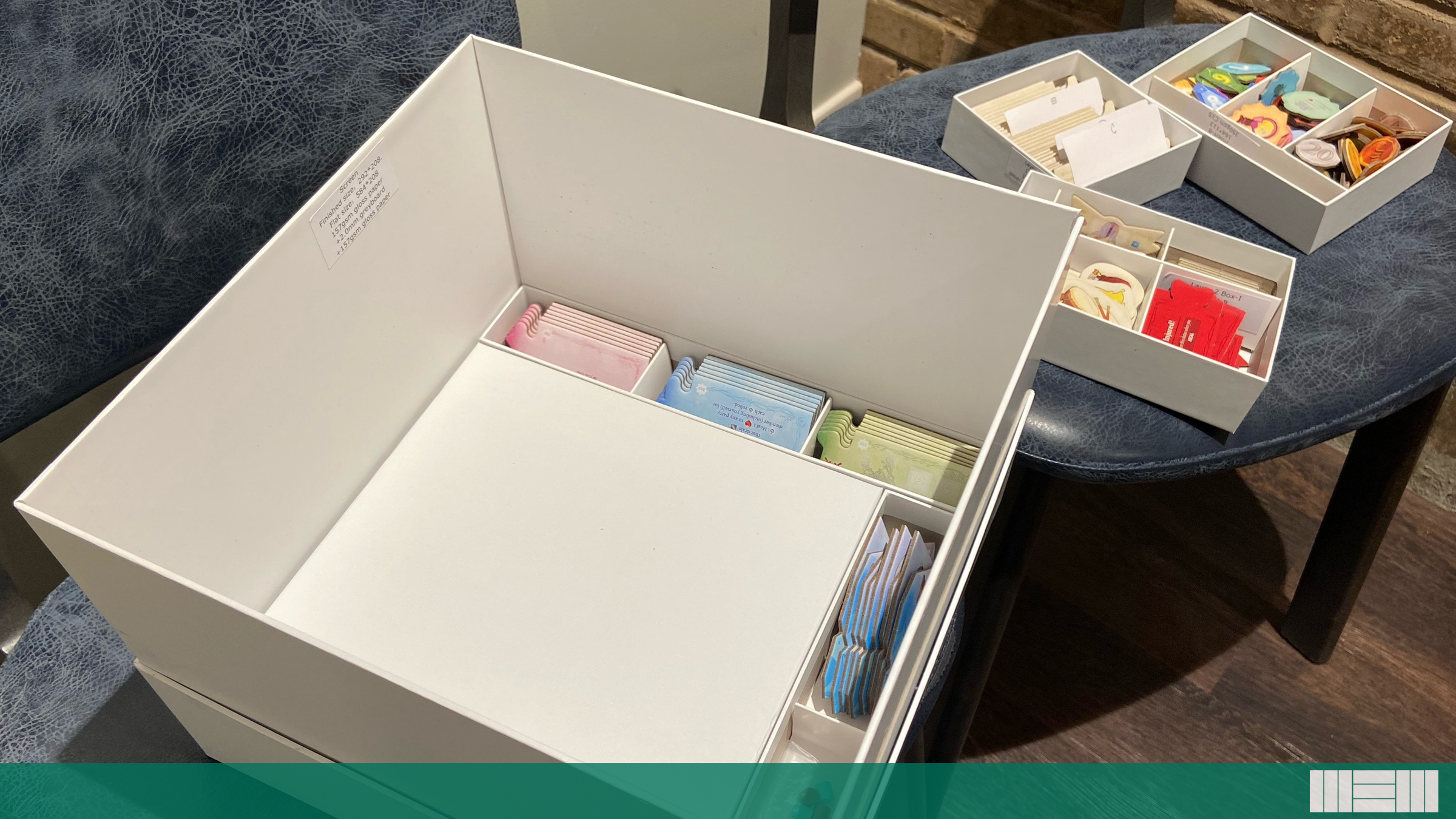 A cardboard box about one foot on each side has a layer of puzzle pieces in it, with other pieces in separate trays that fit inside that box.