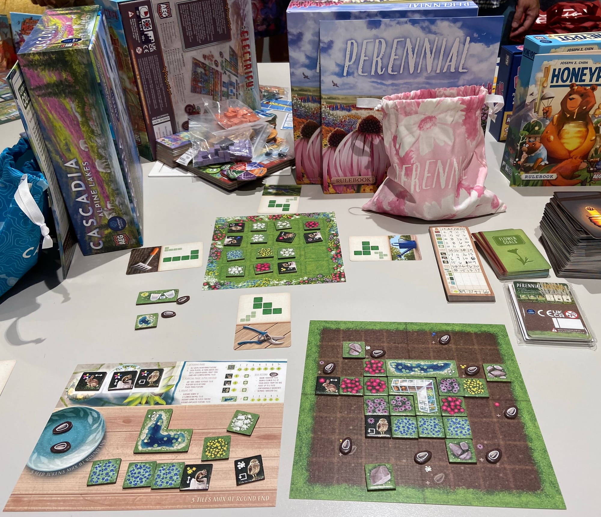 Dozens of square garden tiles are on a personal player board, a holding area, and a shared market grid, along with polygonal tools on playing cards.