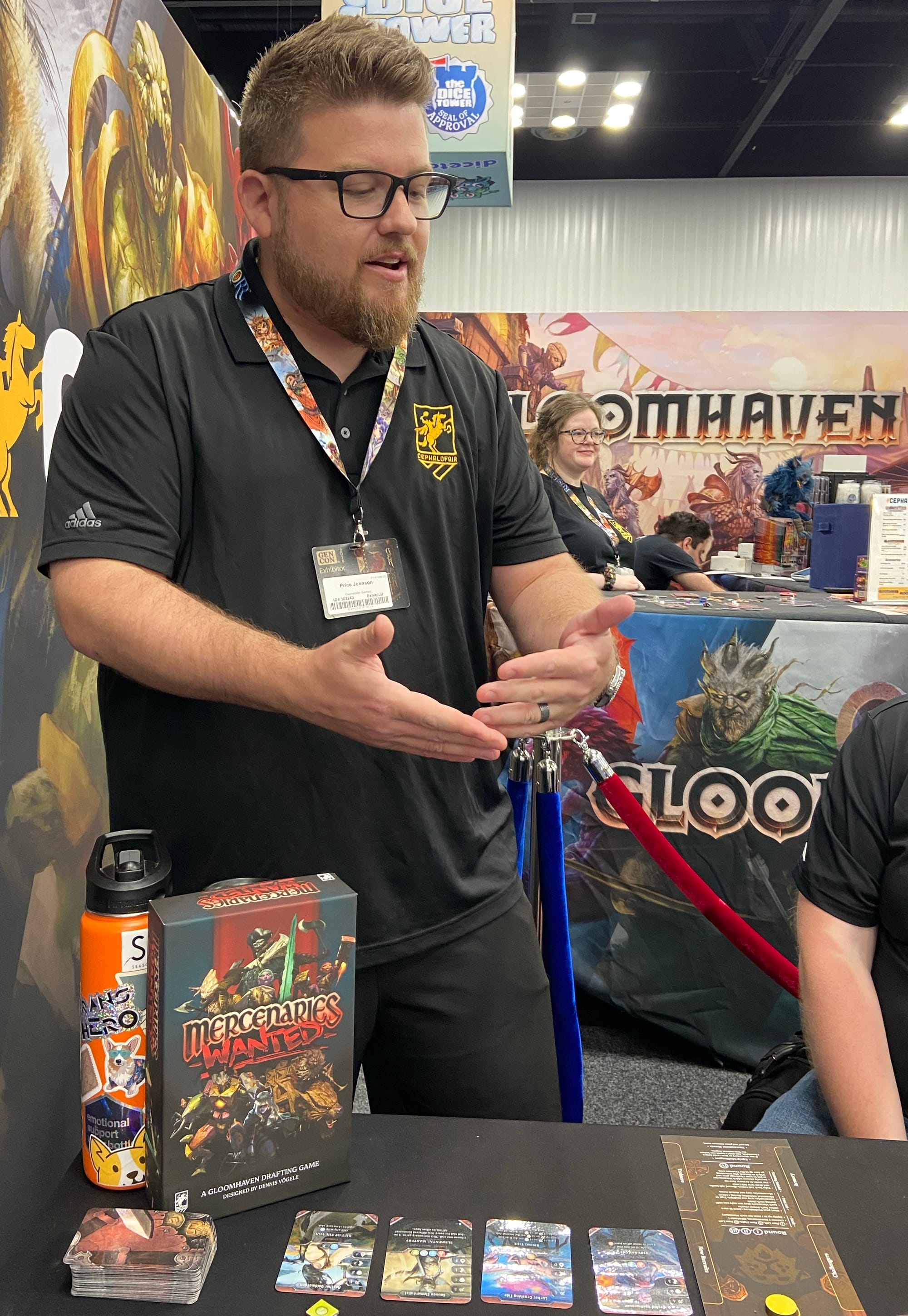 A man gestures with his hands, caught mid-sentence in the Cephalofair Games booth at Gen Con 2026.