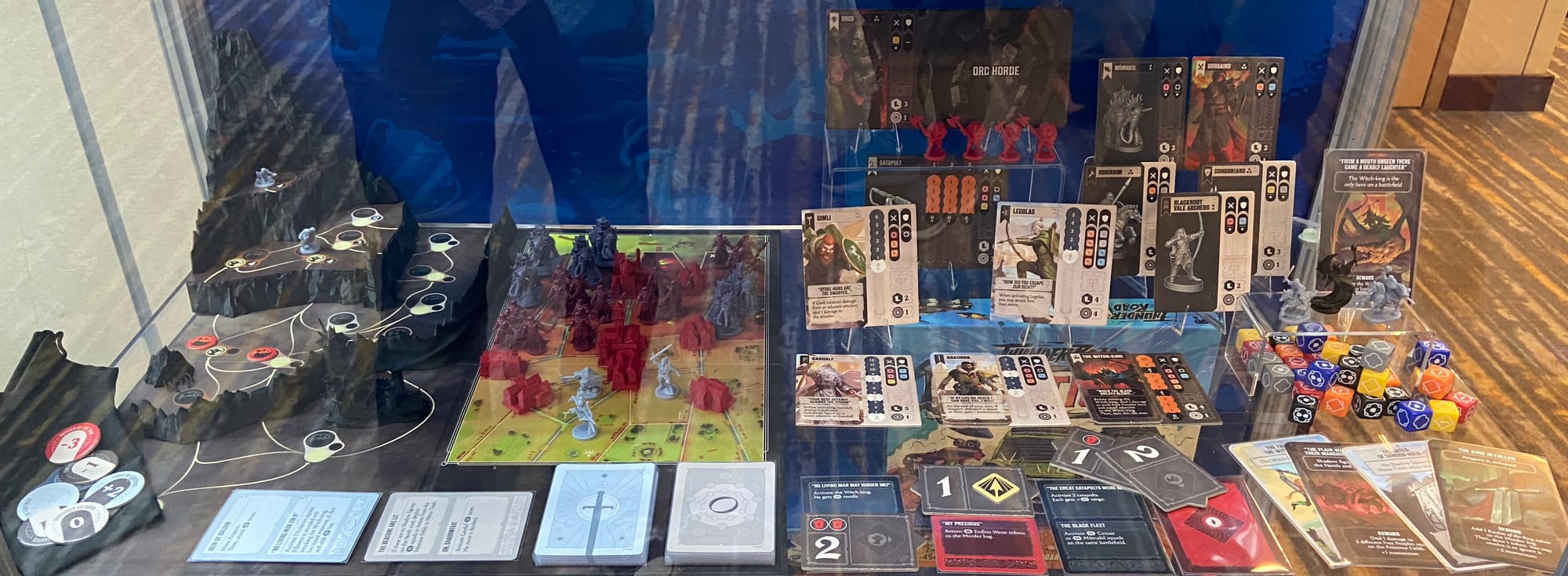 Dozens of cards, tiles, dice, and plastic figures cover a glass shelf.