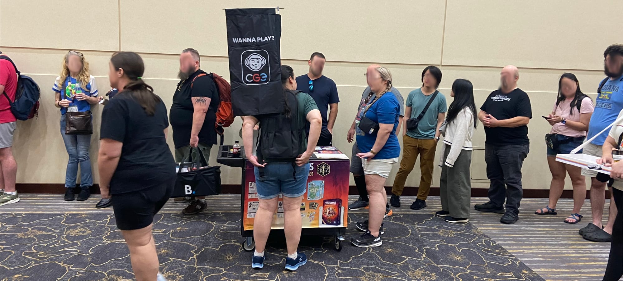 A line of people stand near a portable game display featuring Codenames: Critical Role Adventures