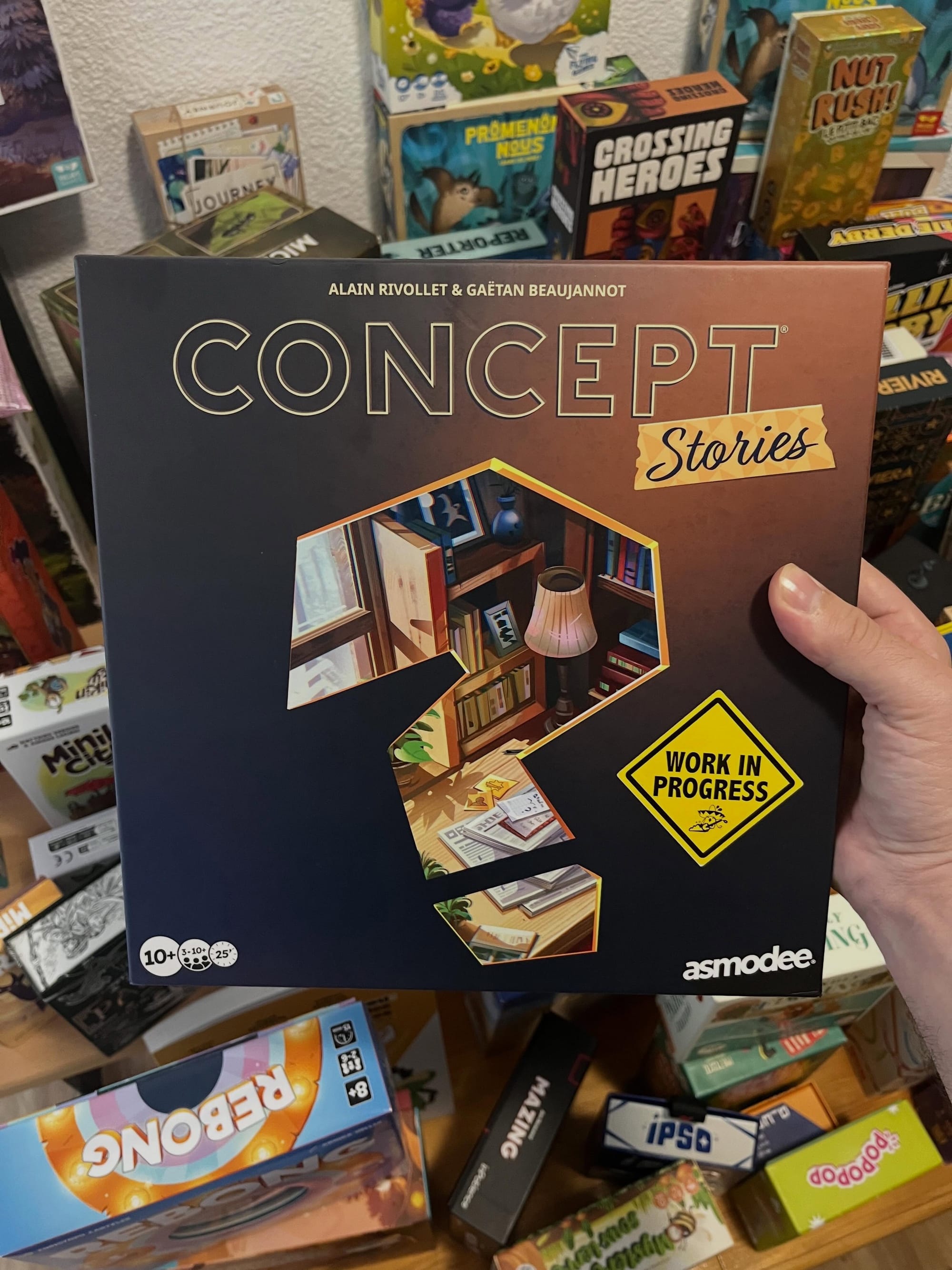 A hand holds a box reading Concept: Stories, with the cover being mostly brown aside from a question mark through which you can see items on a desk.