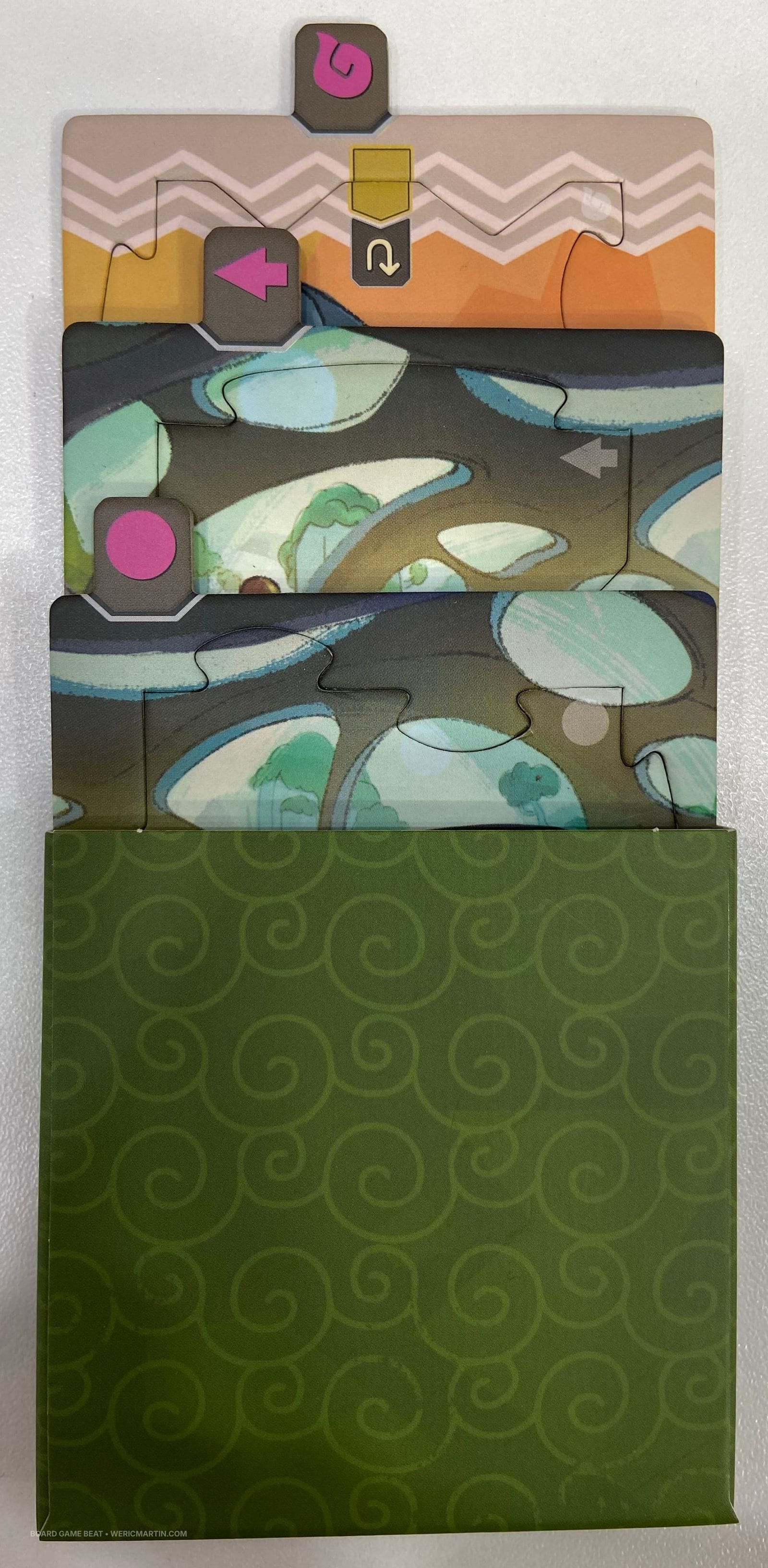 Three cardboard squares that each have a square-ish puzzle in them are halfway puzzled from a cardboard sleeve.