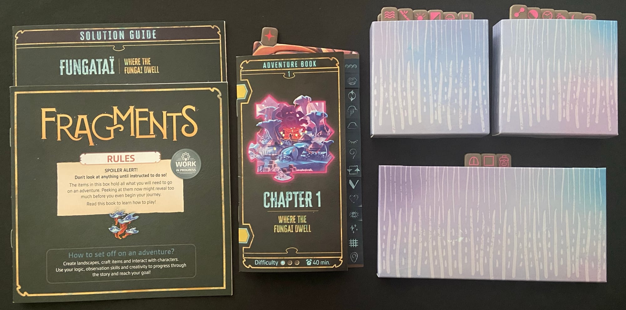 Three wallets filled with cardboard sleeves lie next to the "Chapter 1 Adventure Book", which is next to the rulebook and solution guide.
